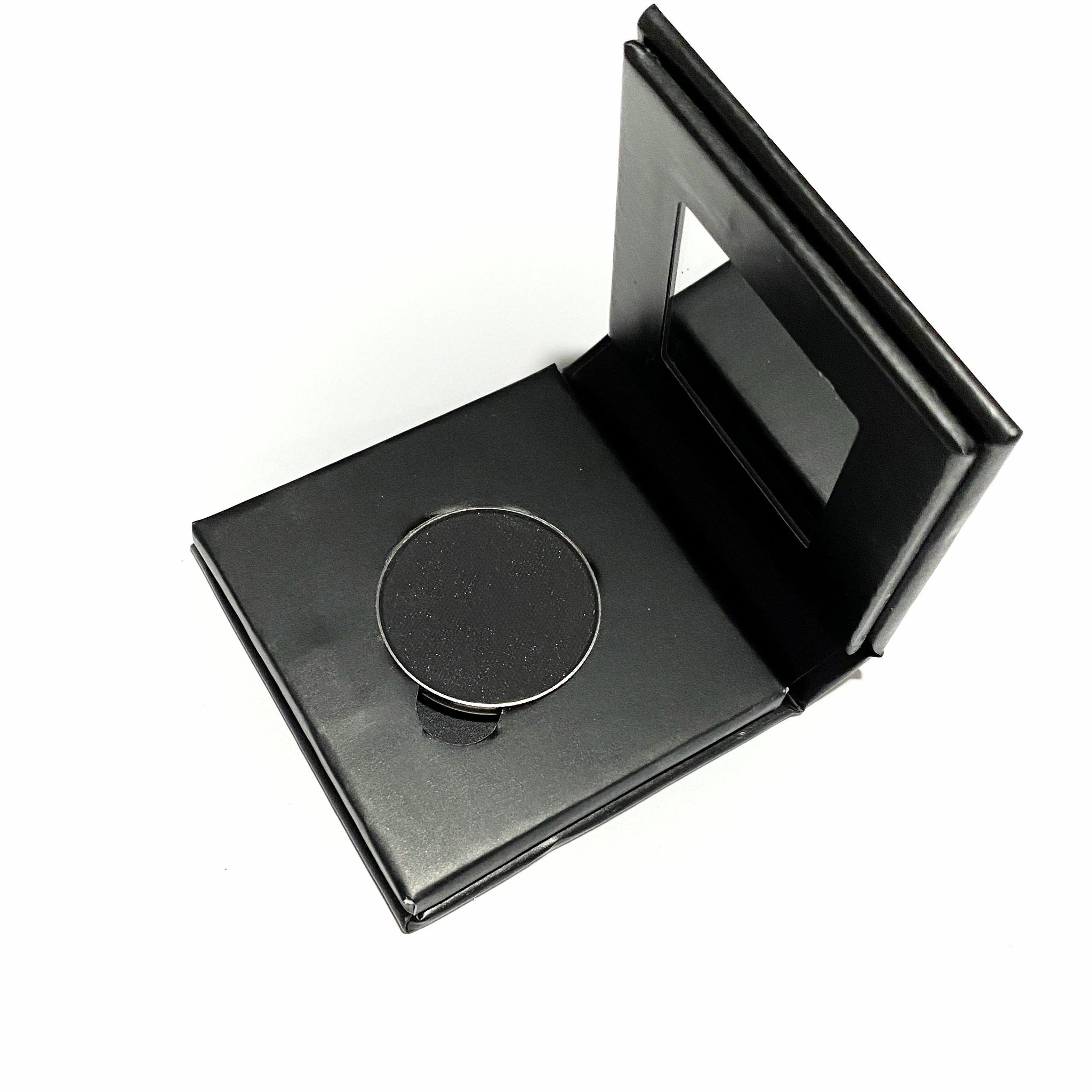 Close-up of jet black mineral eye shadow in matte finish, housed in a sleek paperboard compact.
