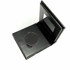 Close-up of jet black mineral eye shadow in matte finish, housed in a sleek paperboard compact.