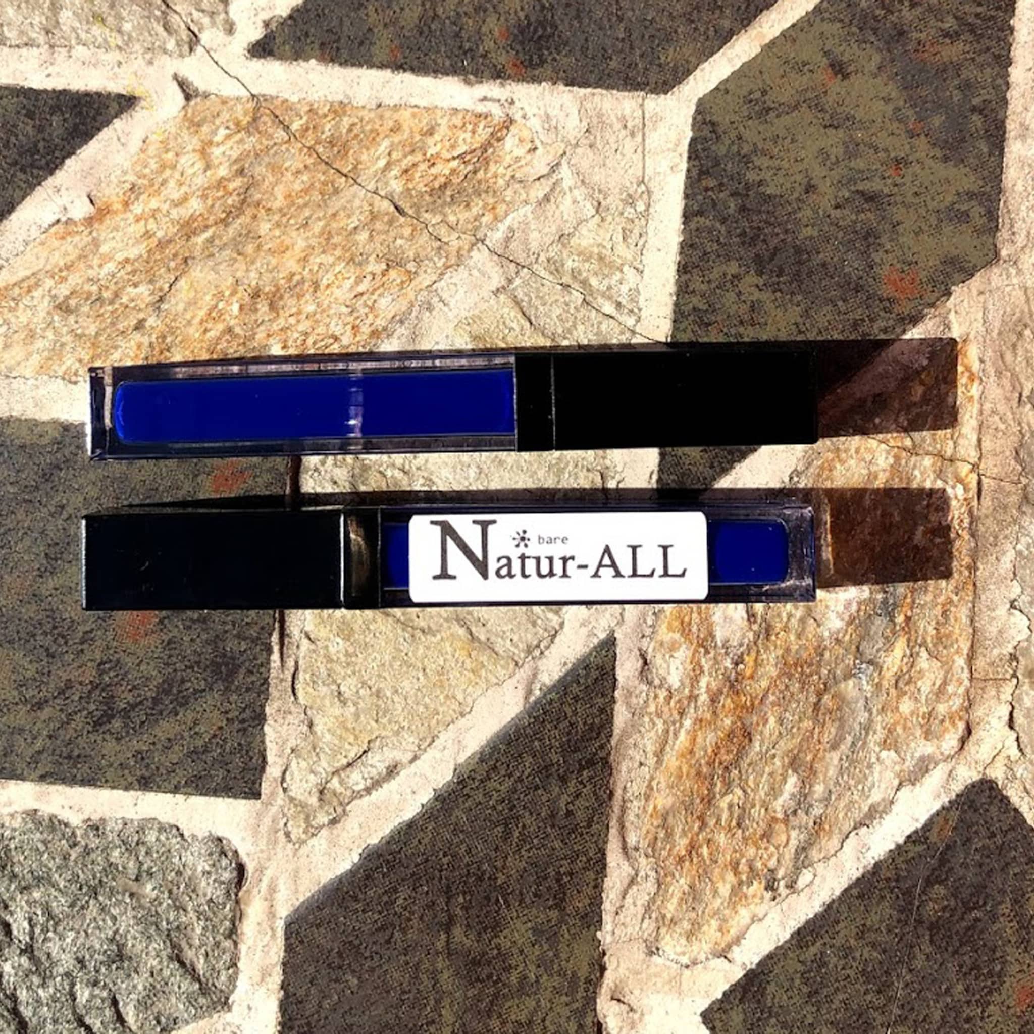 Lip gloss tubes, black plastic, blue liquid, Natur-ALL brand visible on label