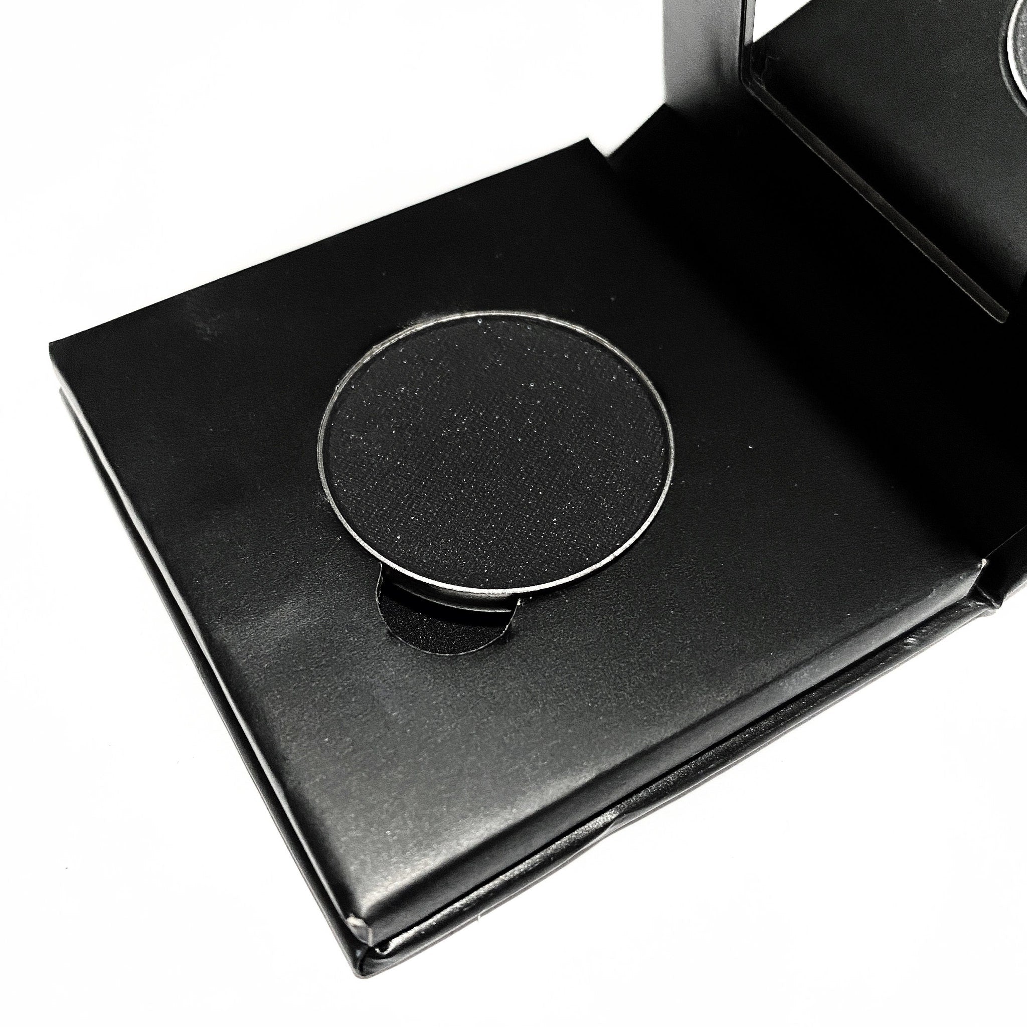 Close-up of matte black pressed mineral eyeshadow with smooth, velvety texture in compact case