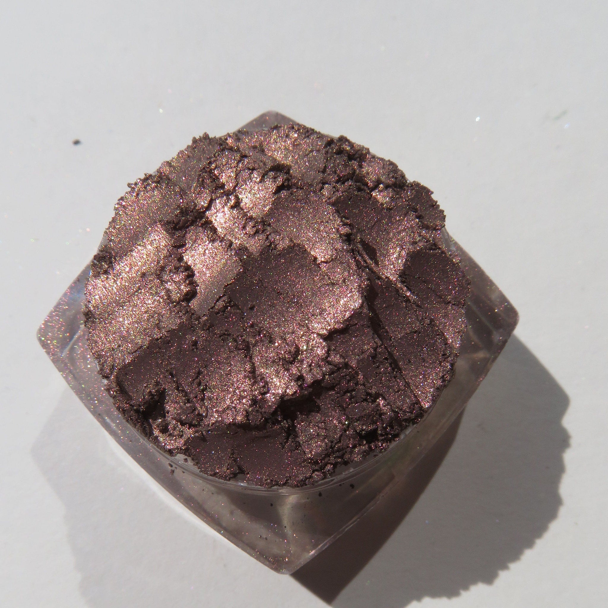 Hand applying shimmering dark brown mineral eyeshadow with rose metallic finish using a fluffy brush