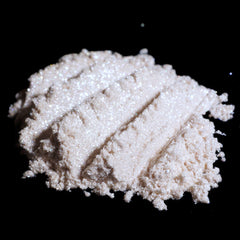 Side view of loose vanilla ivory eyeshadow with silver-white shimmer in transparent jar, showcasing glitter texture