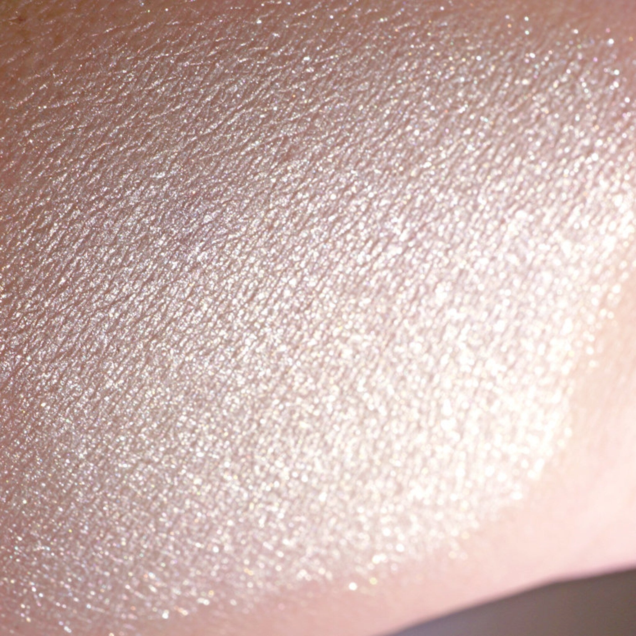 Close-up of loose vanilla ivory eyeshadow with silver and white shimmer particles spilling from jar