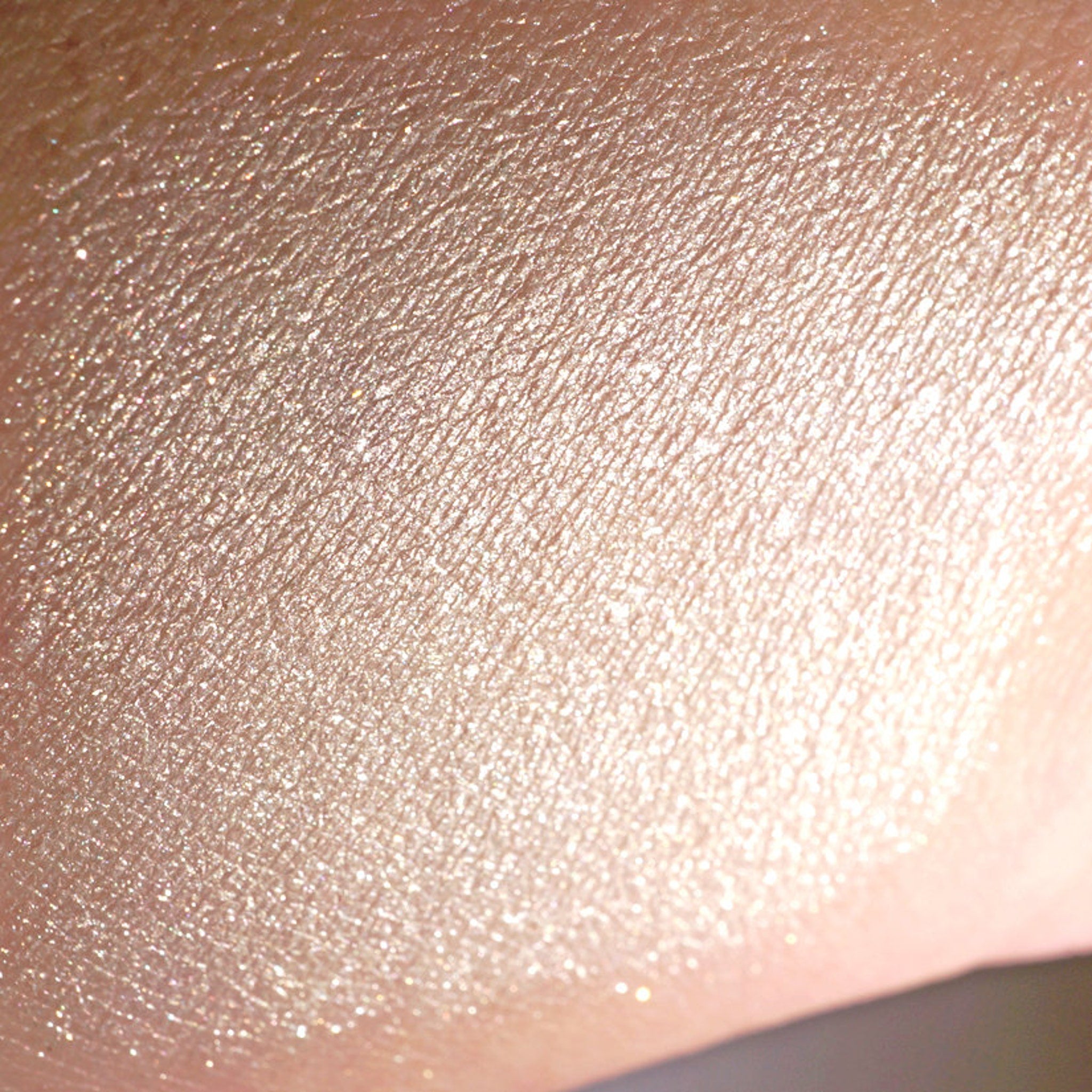 Side view of loose vanilla ivory eyeshadow with silver-white shimmer in a sifter jar, catching light at an angle