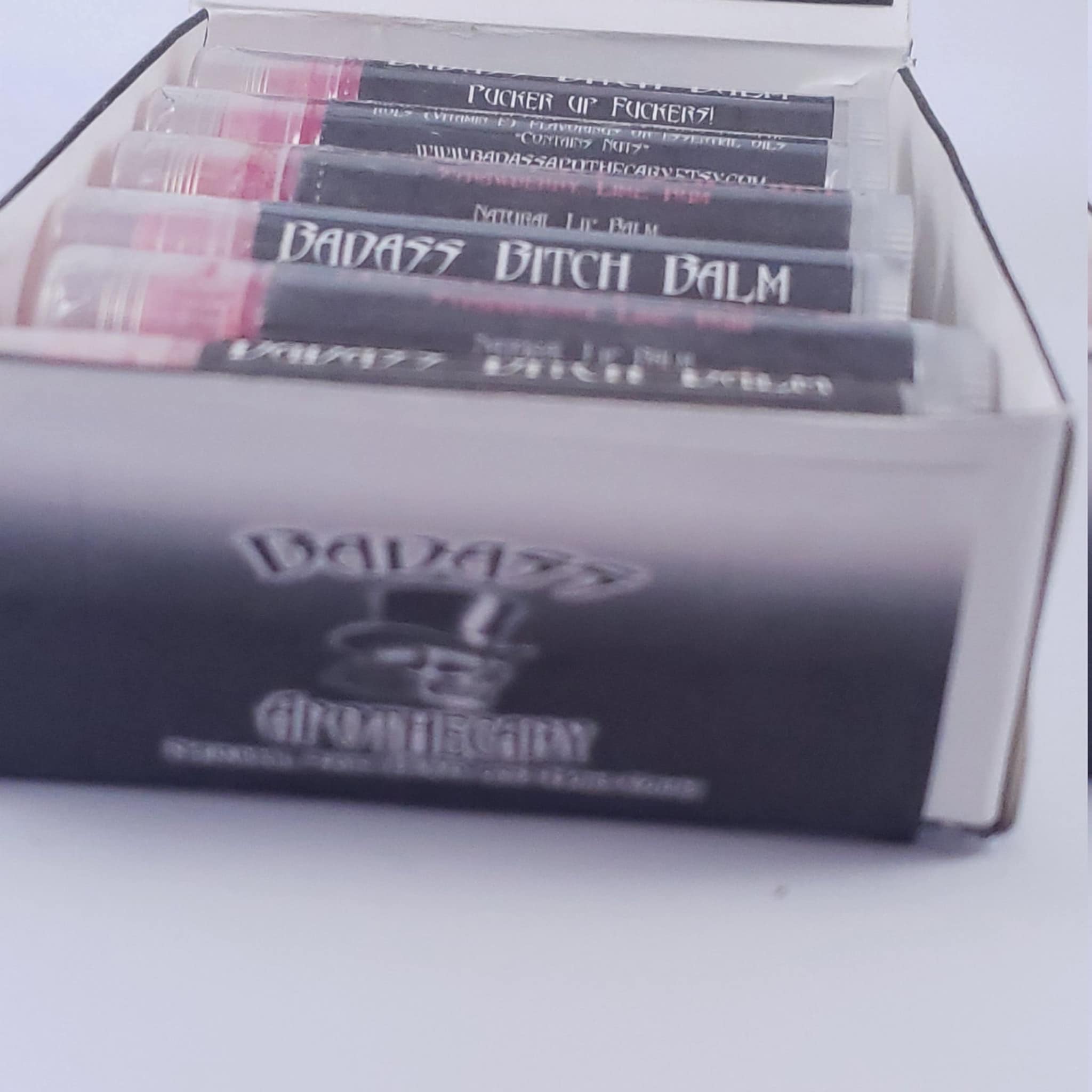 Lip balm tubes with pink tint, black labels, and "BADASS" text in a box