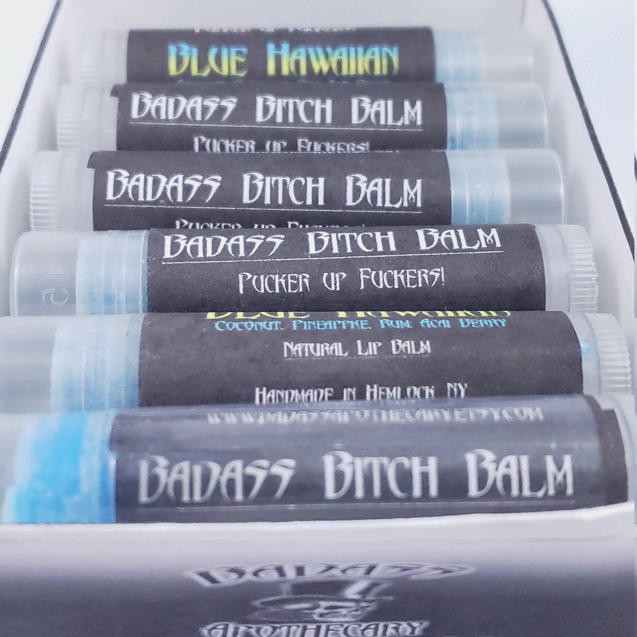 Lip balm tubes with black labels, white text, and blue balm inside, "BADASS BITCH BALM" brand visible