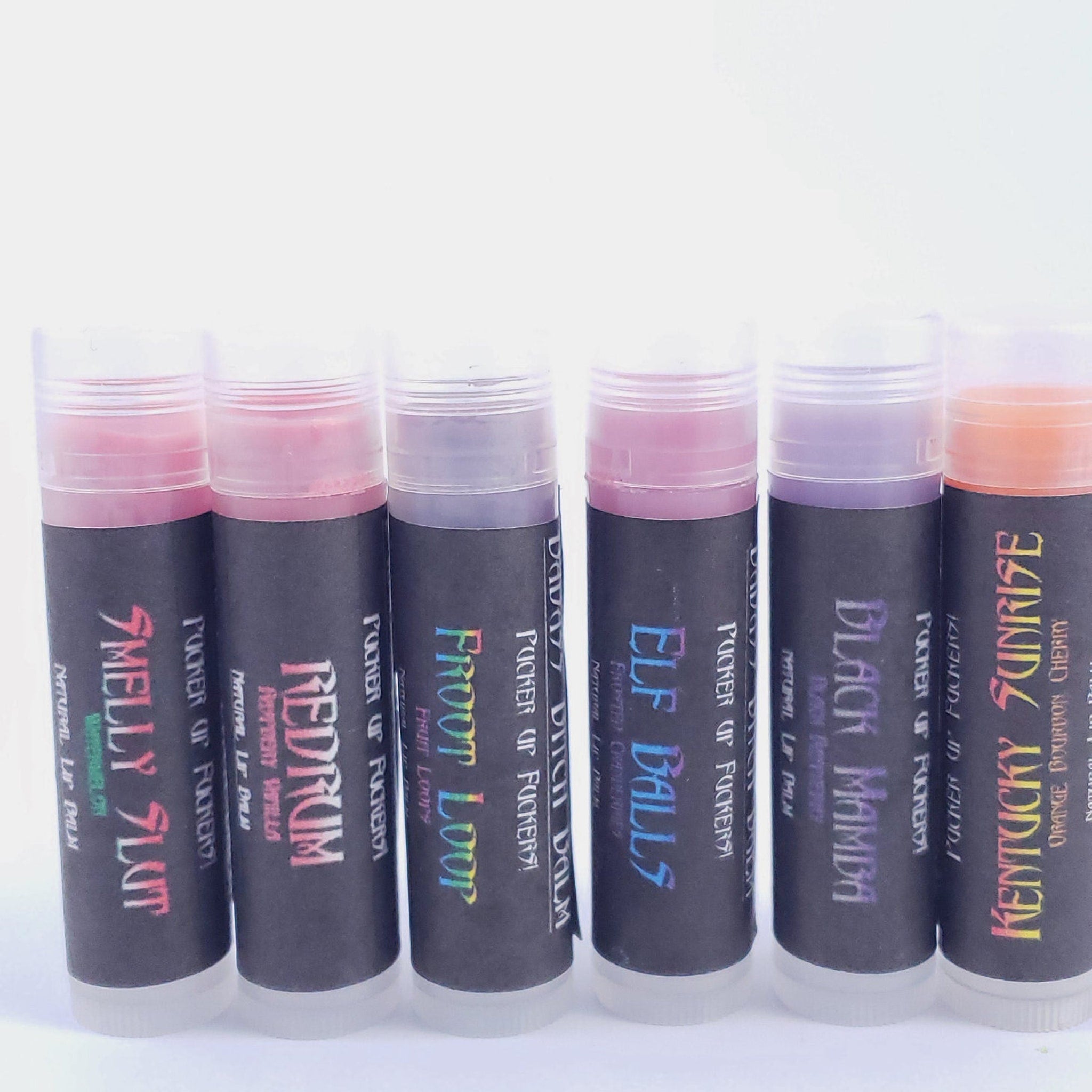 Lip balm tubes with various colors and text labels, clear tube and black label.