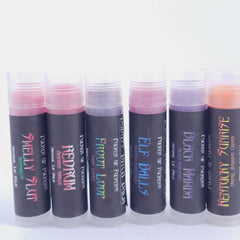 Lip balm tubes with various colors and text labels, clear tube and black label.