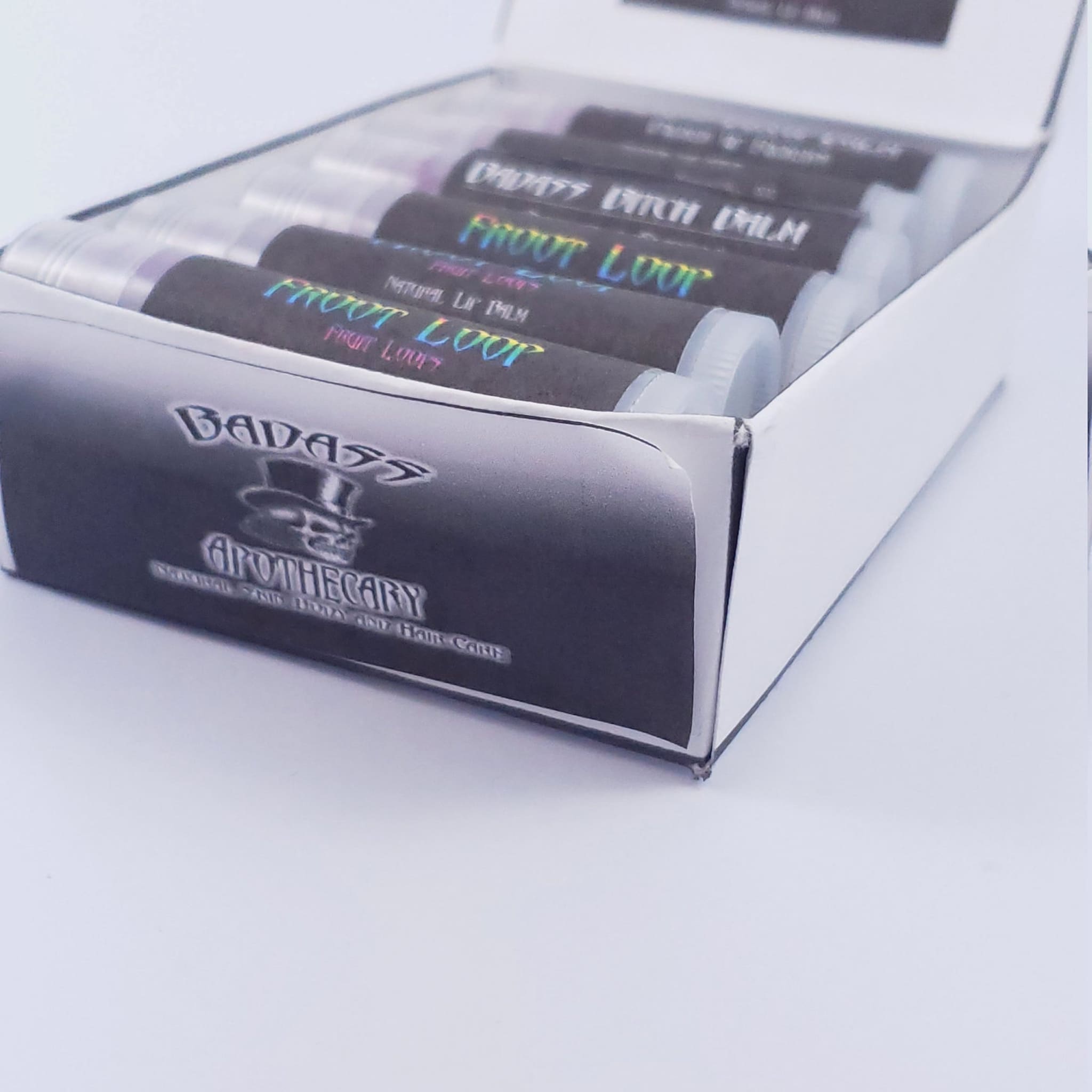Lip balm tubes with black and holographic labels, in a white box, Badass Apothecary brand