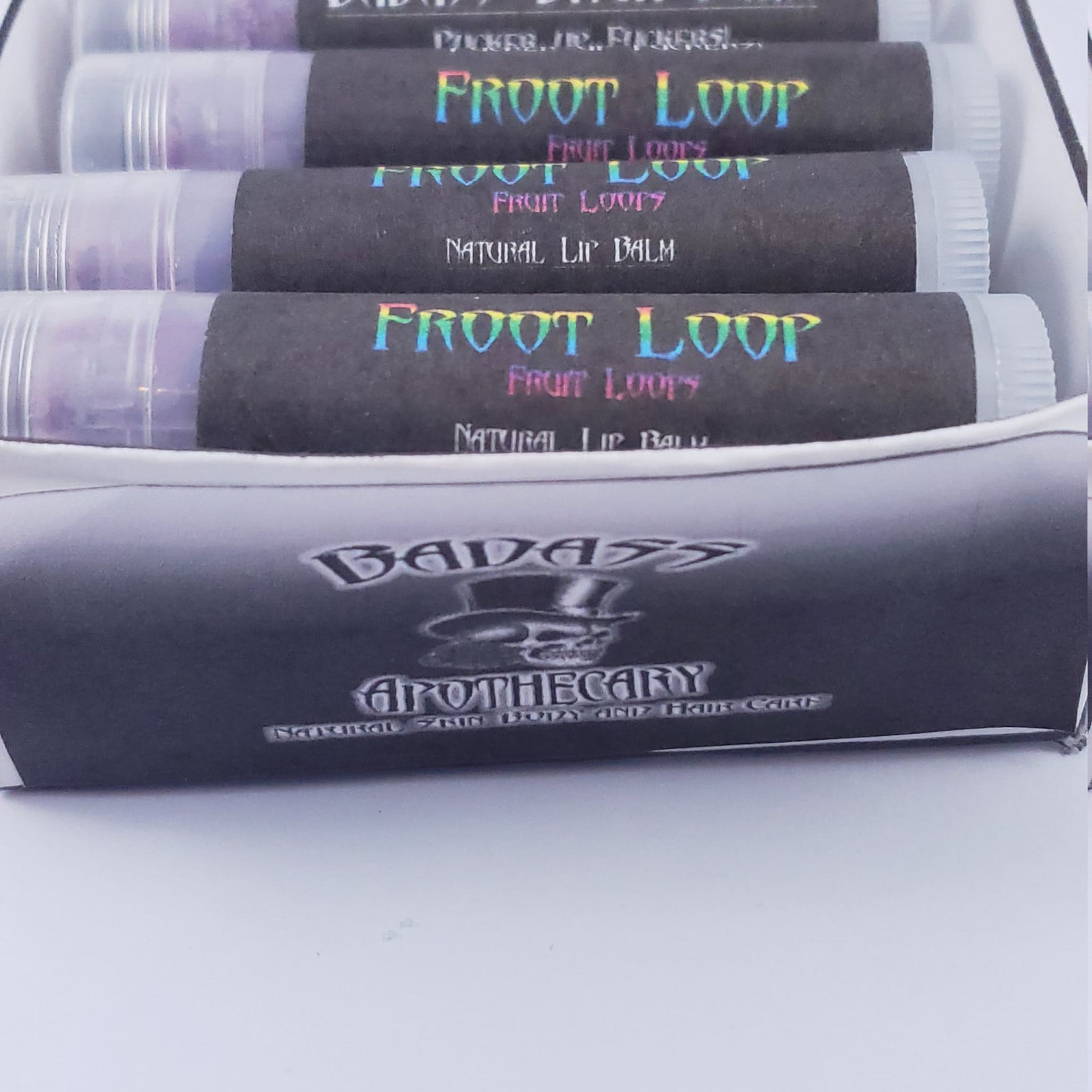 Lip balm tubes with black labels and "Froot Loops" text, clear plastic tubes, white box