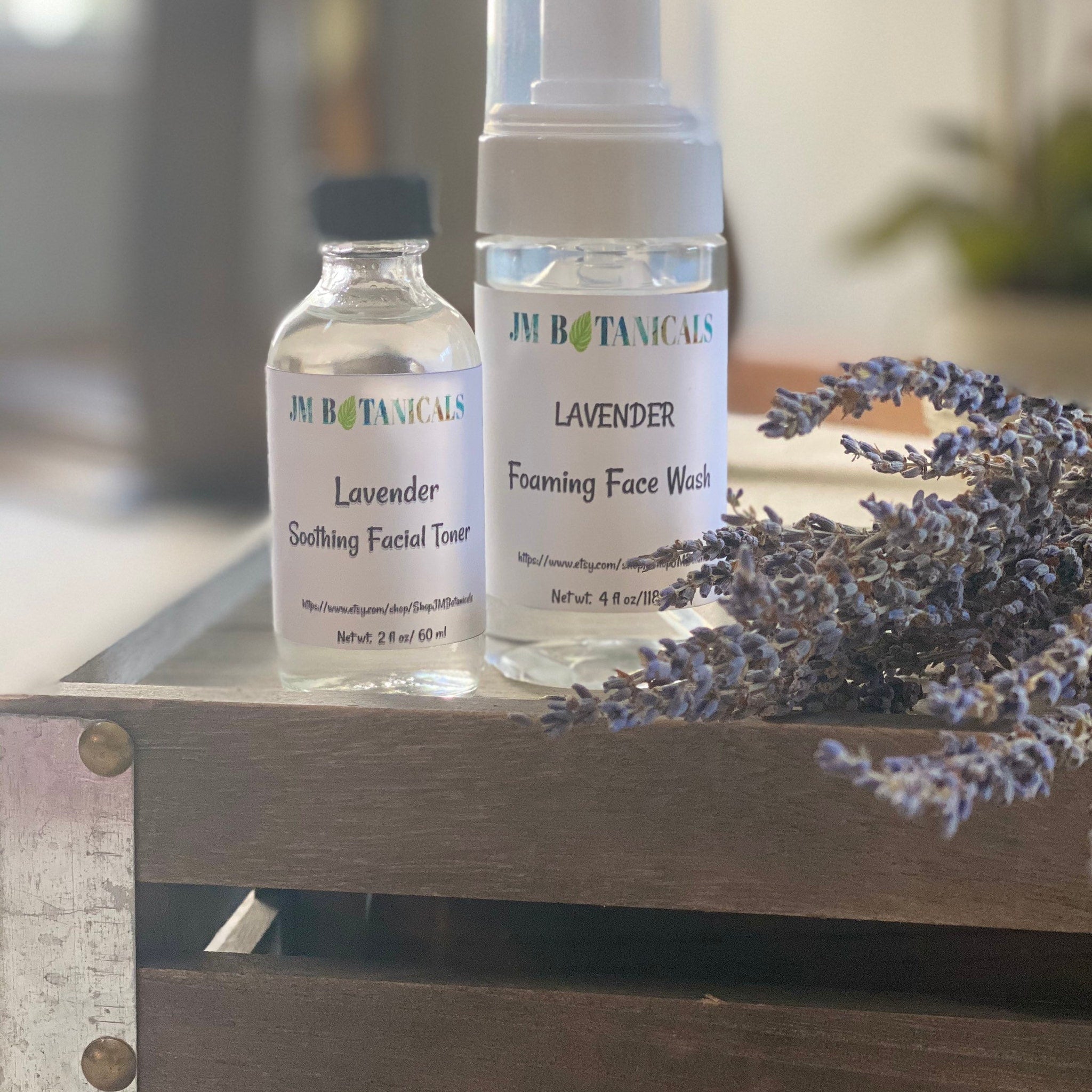 Lavender toner and face wash bottles with JM Botanicals label, clear glass, and lavender sprig on wooden tray