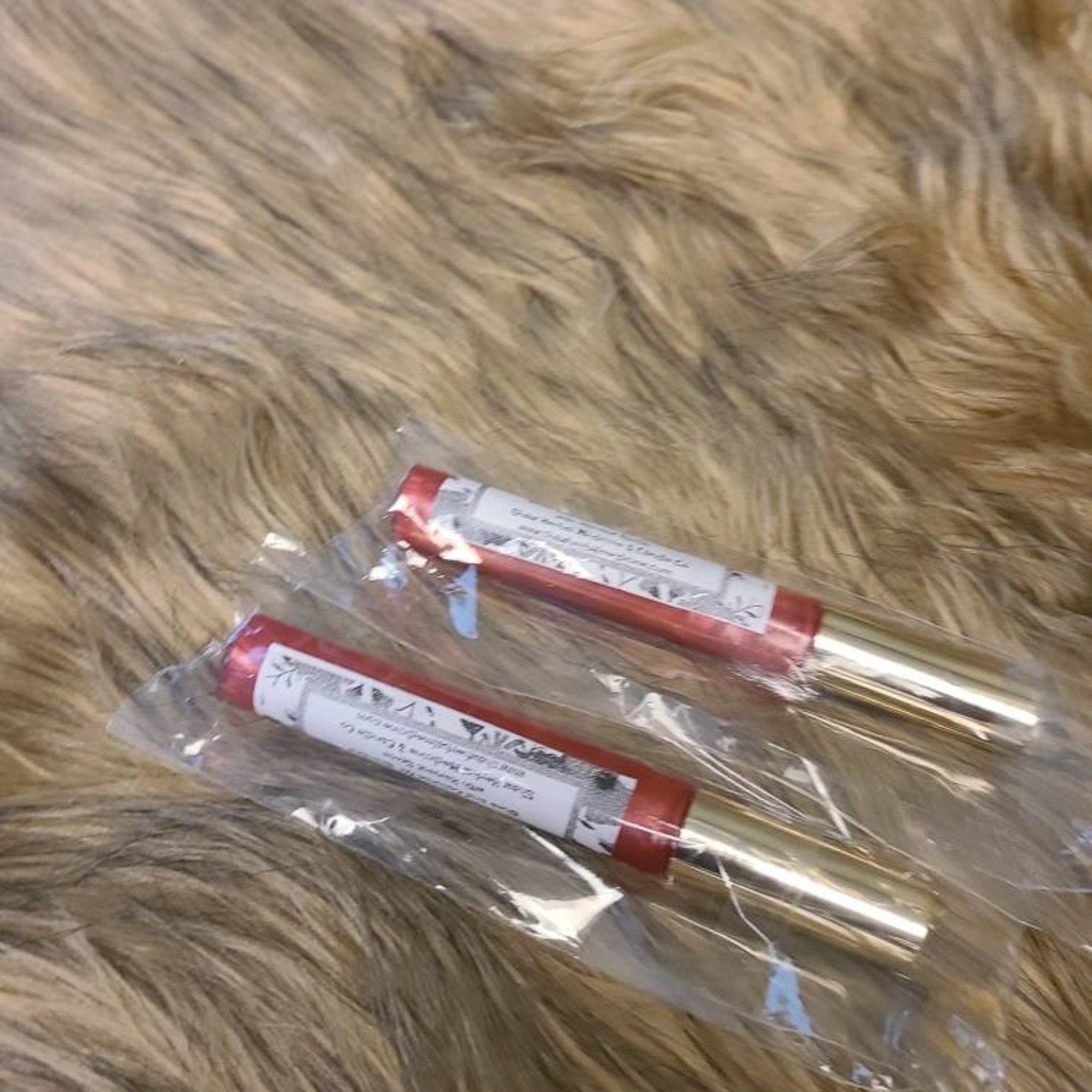 Lip gloss tubes with red, gold, and clear packaging on fur background.