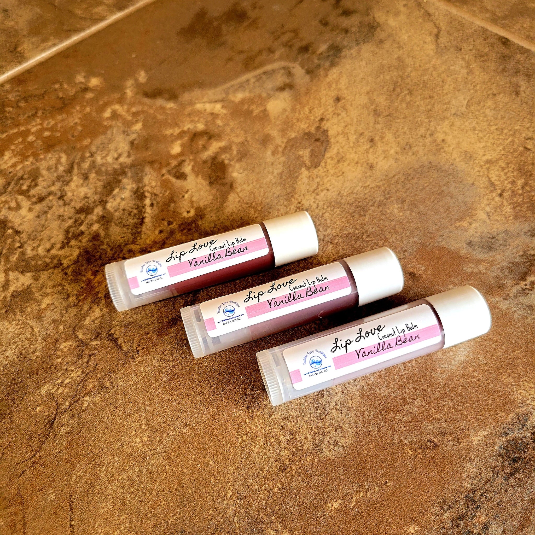 Lip balm tubes with white caps, pink label, and Bubble Love Boutique branding on a brown surface