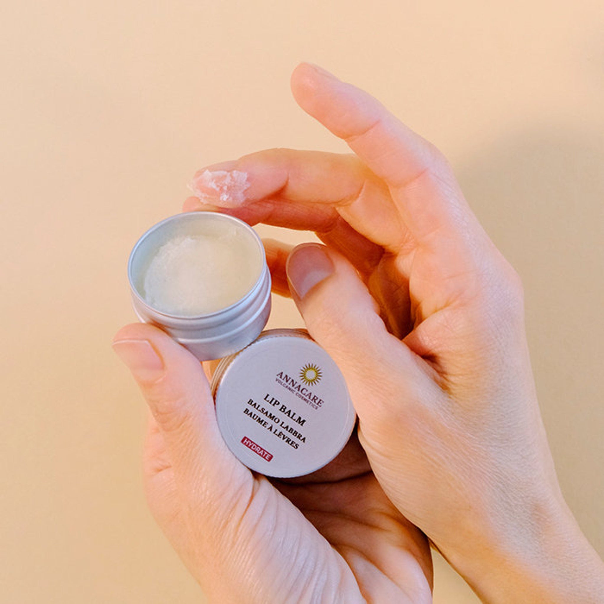 Lip balm in silver tin, white balm, and hands holding product with Annacare label visible