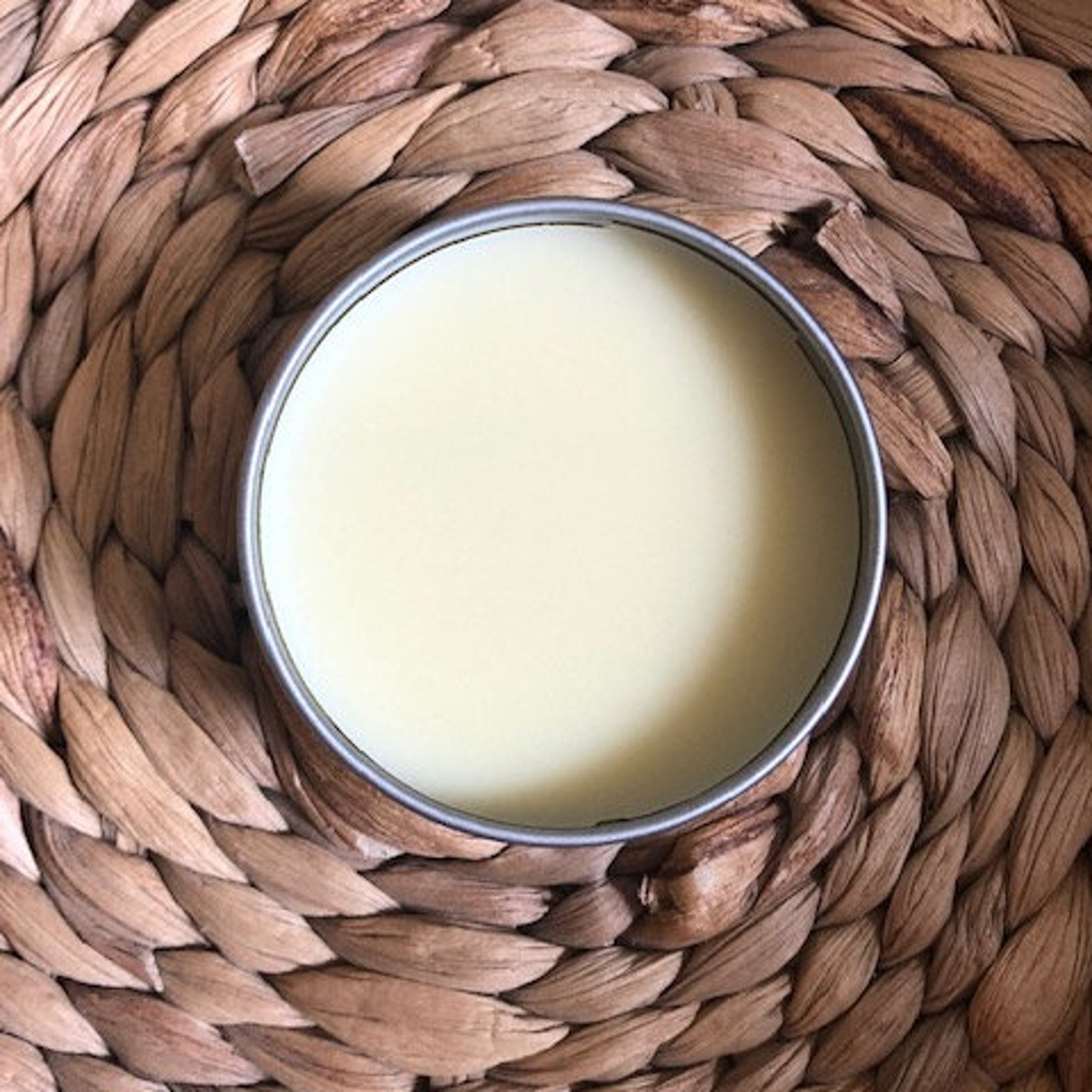 Skin care ointment in silver tin with pale yellow salve on woven brown surface