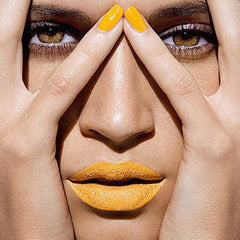 Yellow lipstick and nail polish on face with hands, close up view of eyes and mouth.