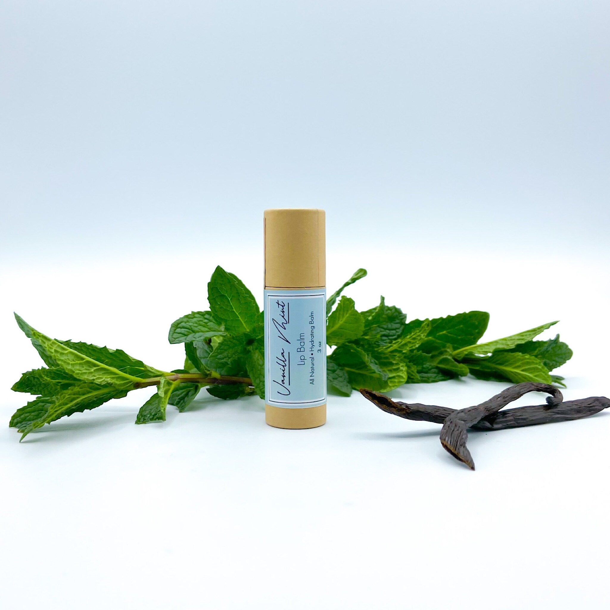 Lip balm tube with tan paper, blue label, and green mint leaves in background
