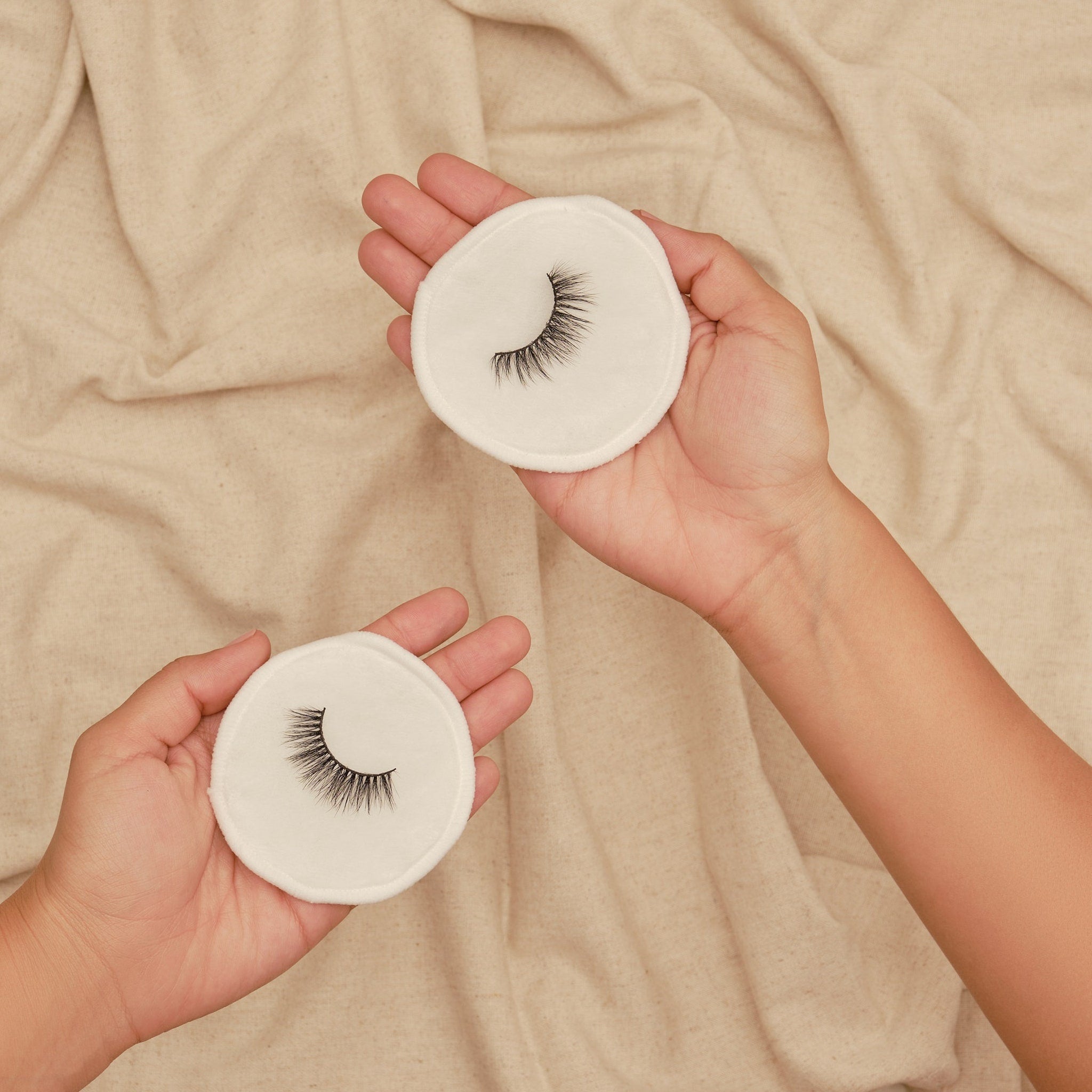 False eyelashes on white cotton pads, black lashes, held in hands, beige background