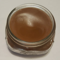 Brown liquid in a clear glass jar with a metal rim, sitting on a white surface
