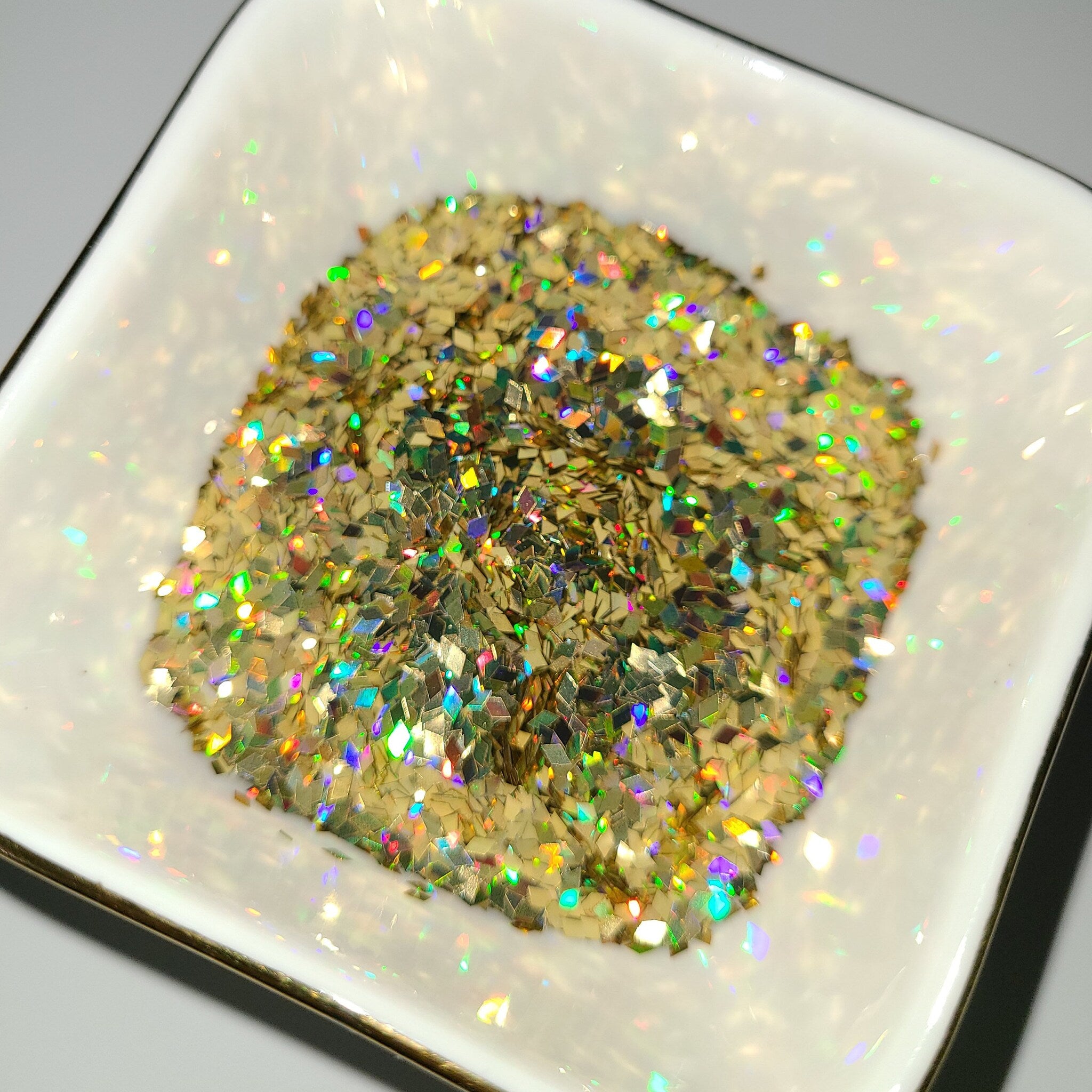 Gold glitter flakes with iridescent sparkle in a white square dish with a gold rim