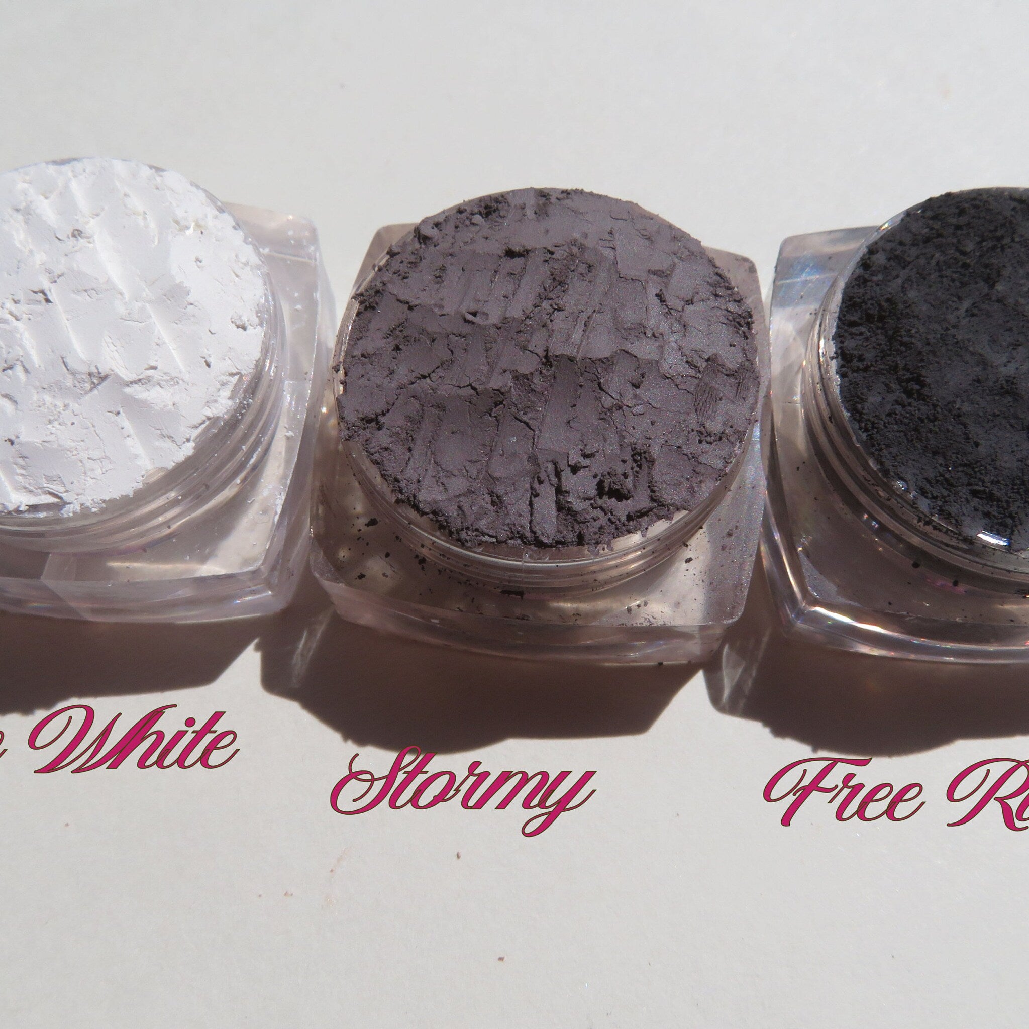 Side view of four vegan loose mineral eyeshadows in glass jars with sifter lids, showcasing texture and shimmer