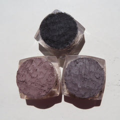 Close-up of four loose mineral eyeshadows in glass jars showing shimmering pink, bronze, taupe, and plum shades