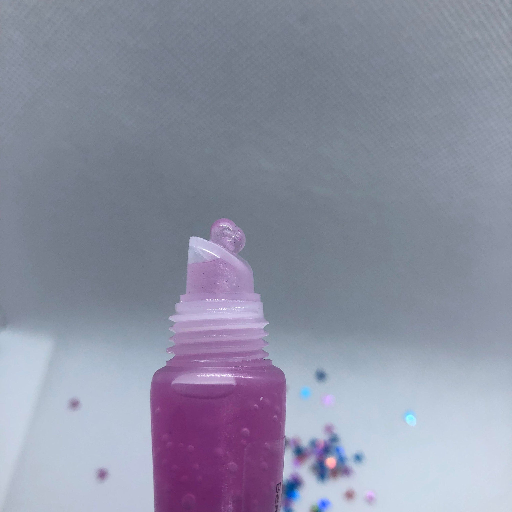Lip gloss tube with purple liquid, clear applicator, and glitter accents.