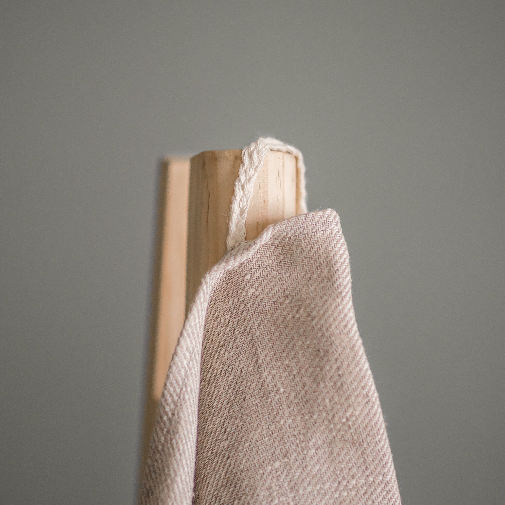 Beige woven fabric with white rope loop, hanging on wooden post