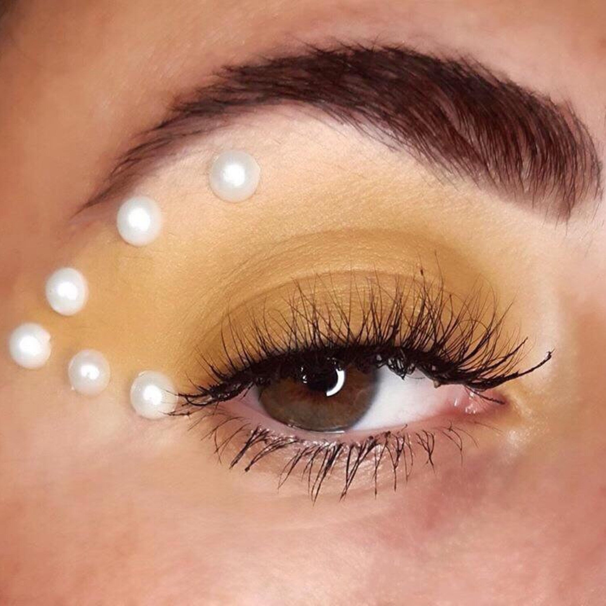 Eye makeup with yellow eyeshadow, white pearls, and long black eyelashes