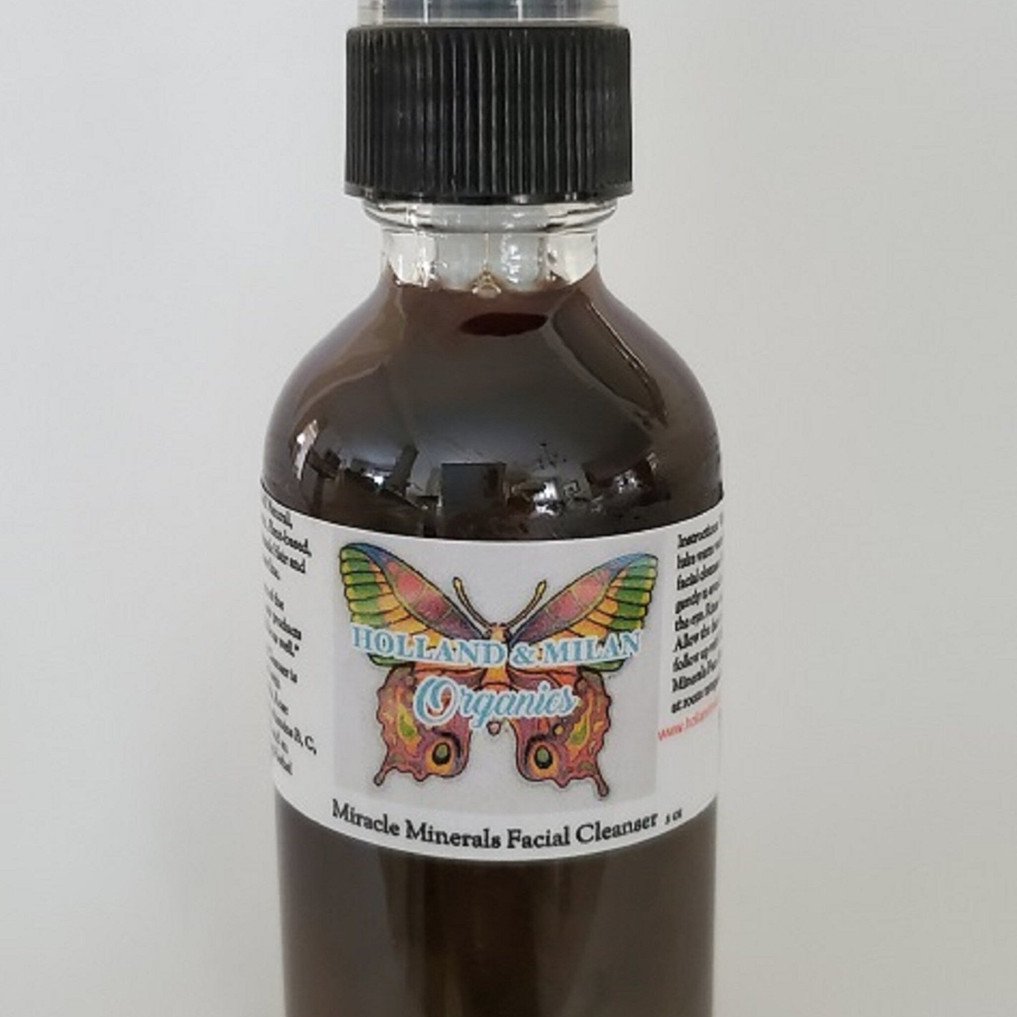 Facial cleanser spray bottle, brown liquid, black cap, Holland & Milan Organics label