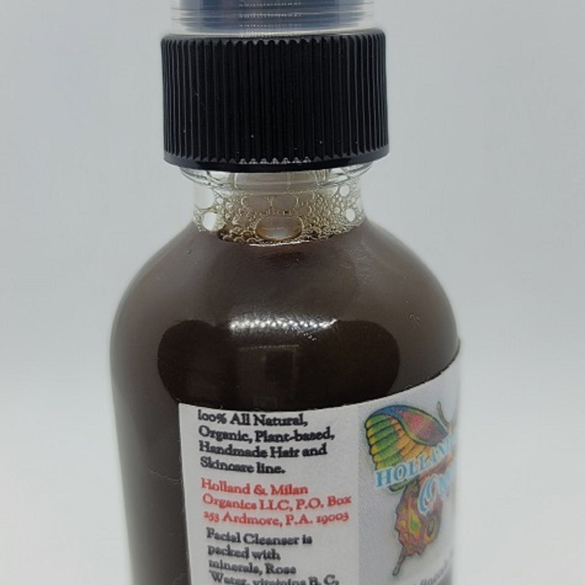 Facial cleanser bottle with black cap, brown liquid, and Holland & Milan label