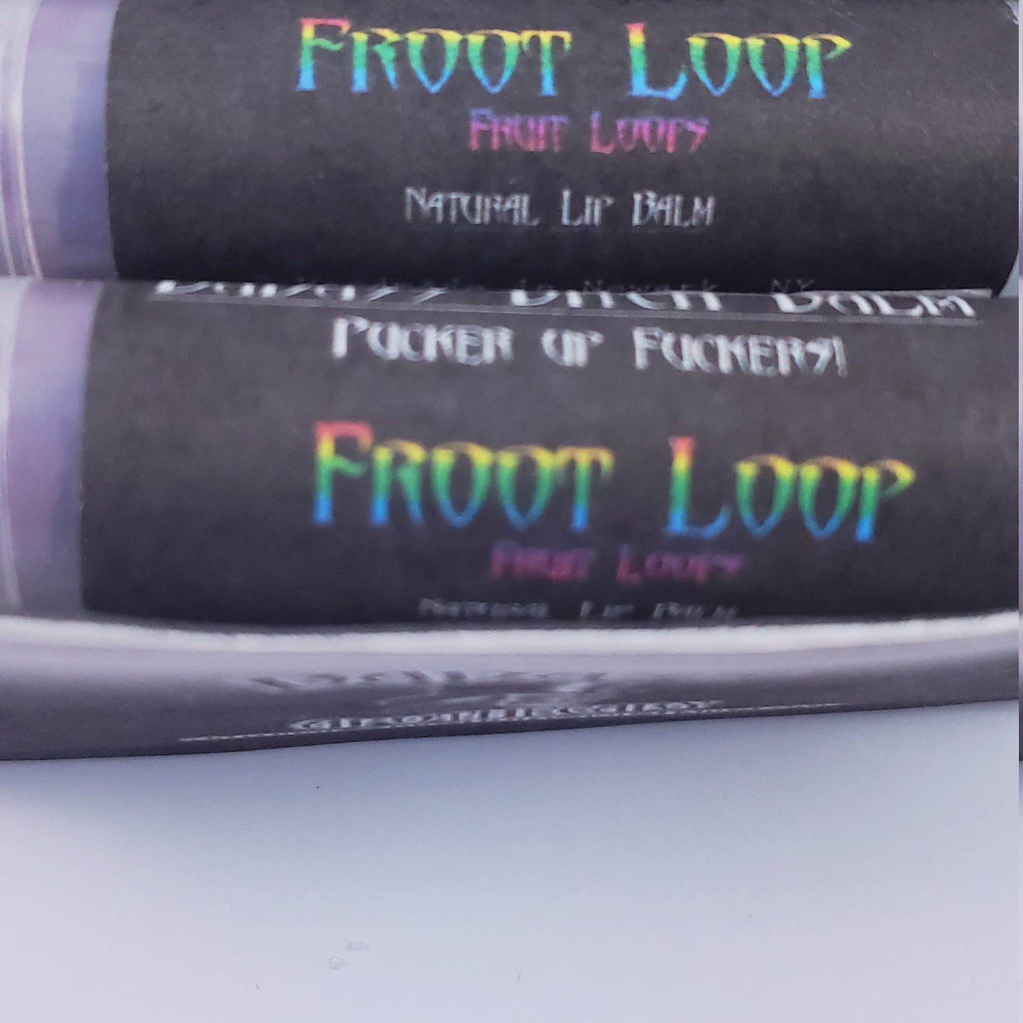 Lip balm tubes with black and purple packaging, rainbow text reading "FROOT LOOP" and "FRUIT LOOPY