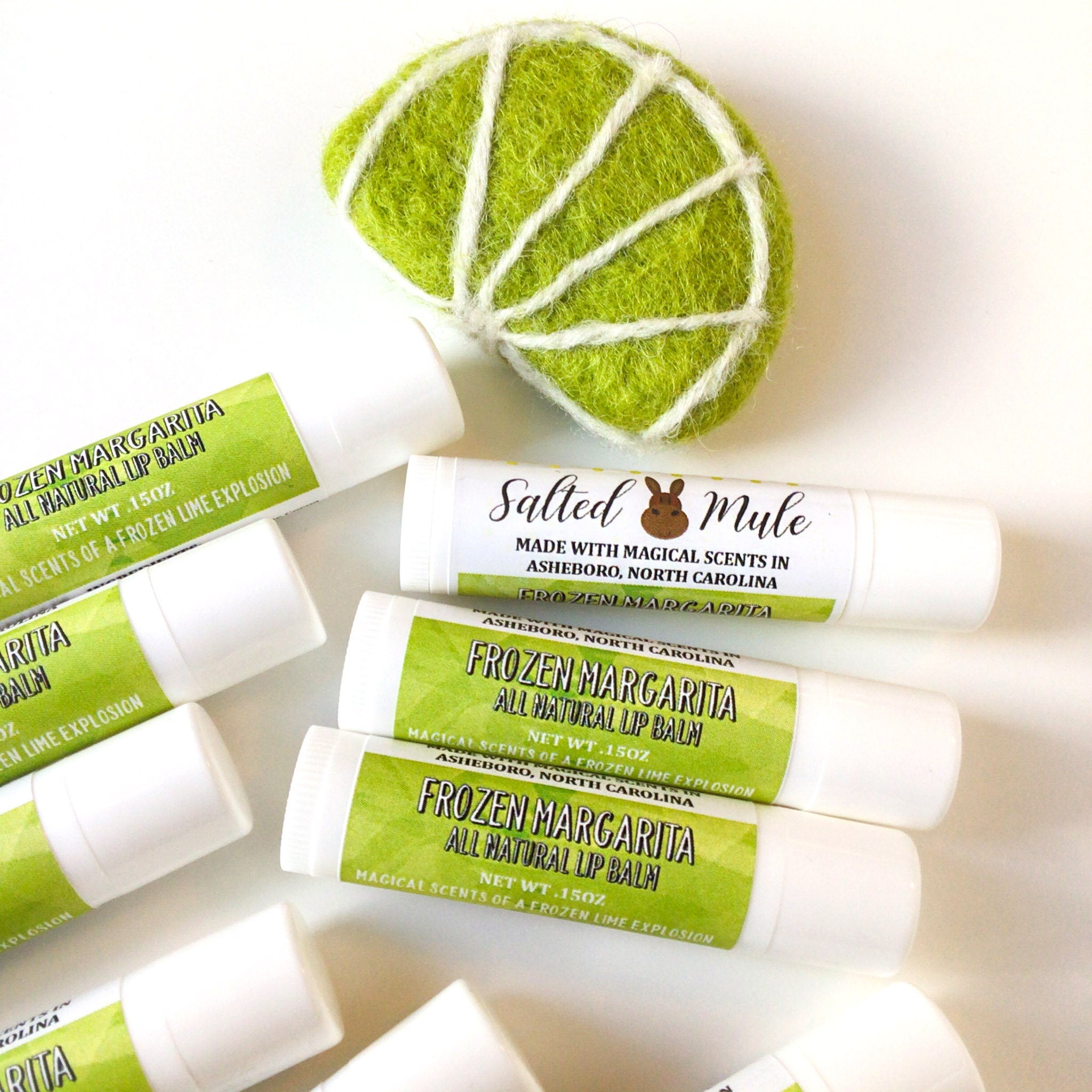 Lip balm tubes with white and green labels, and a lime slice felt decoration on white surface.