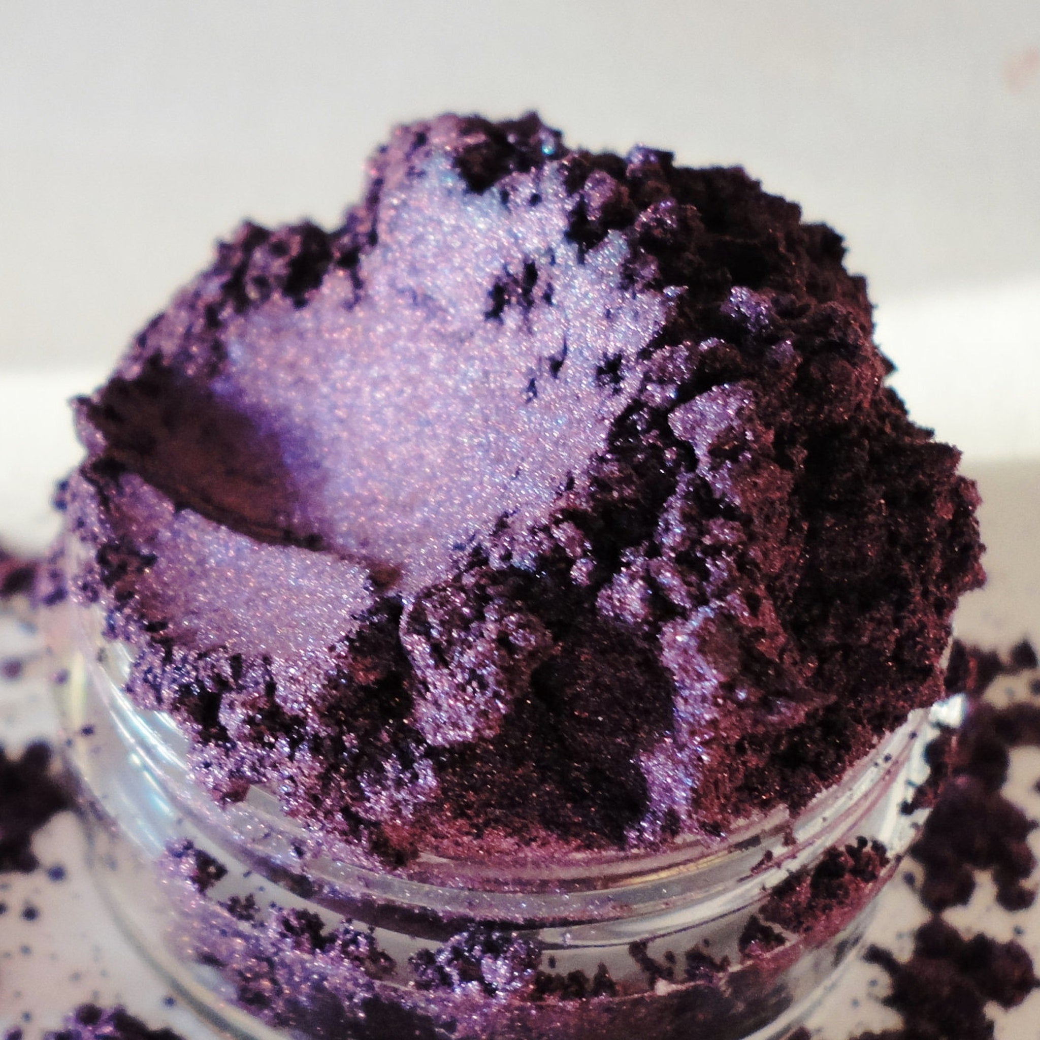 Purple eyeshadow powder with glitter, in a clear jar, close-up view