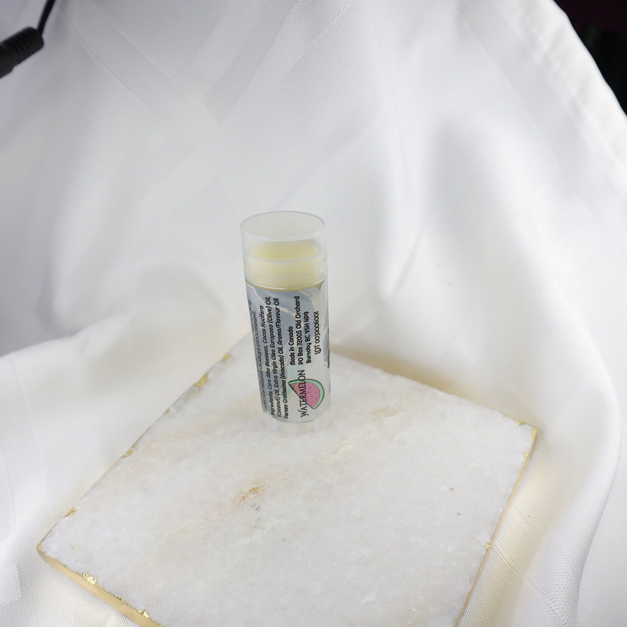 Lip balm tube with clear plastic, yellow balm, and watermelon label on white marble surface