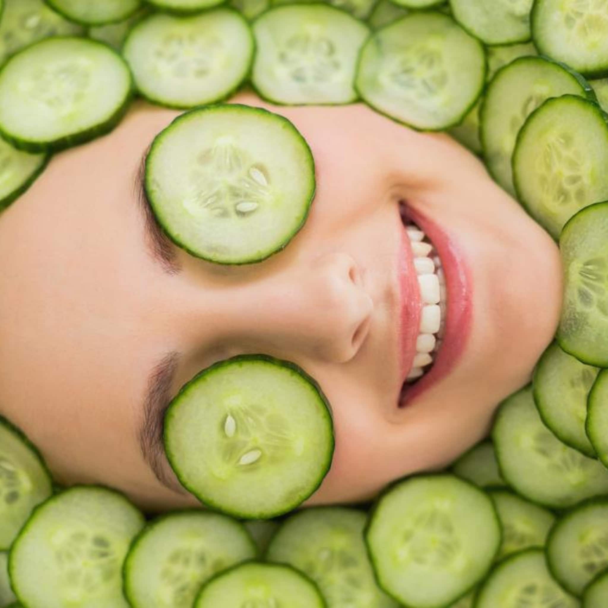 Cucumber slices on face, green and white round slices, smiling woman with cucumbers on eyes