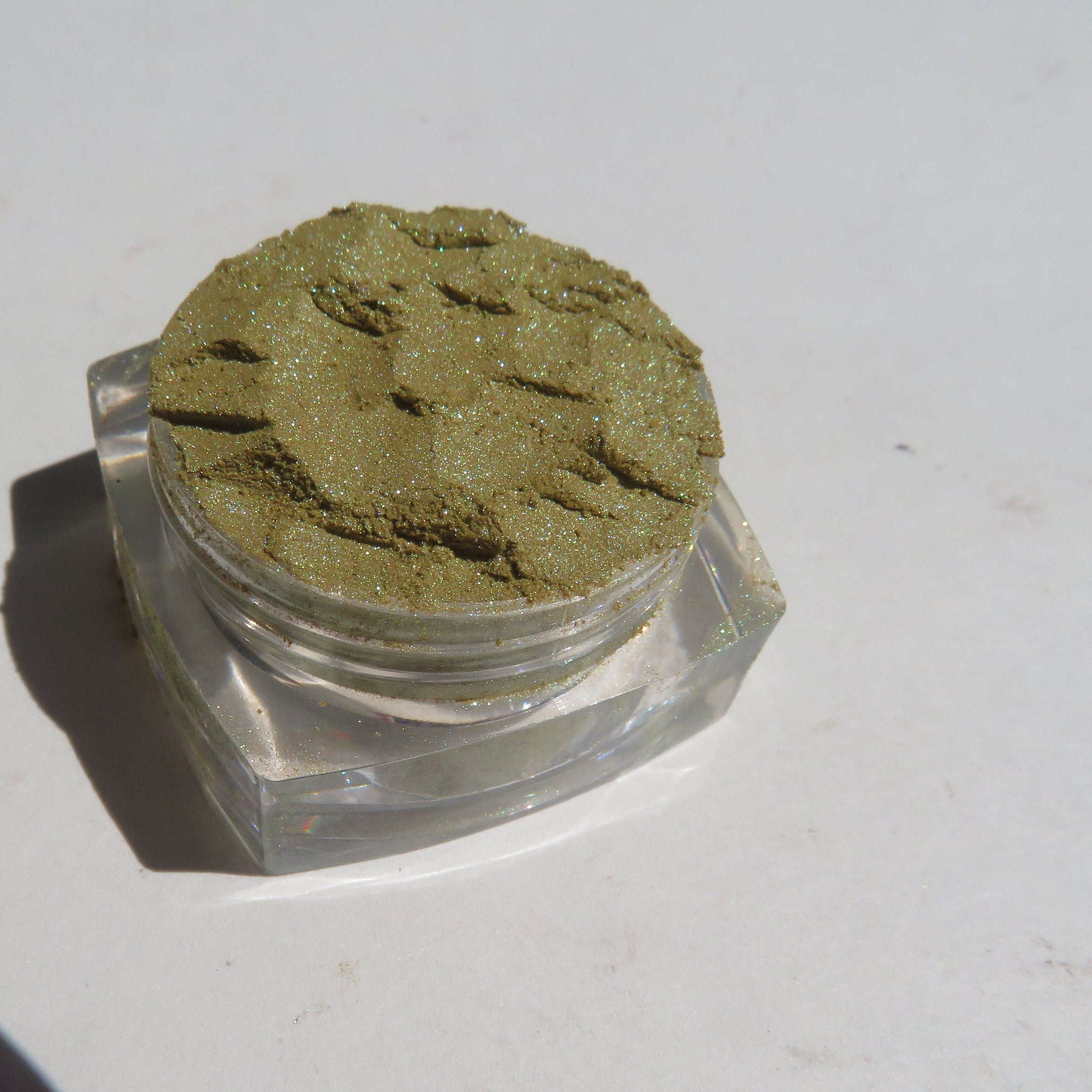 Close-up of loose shimmer eyeshadow powder in vibrant green and gold hues with metallic finish