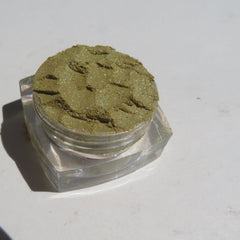 Close-up of loose shimmer eyeshadow powder in vibrant green and gold hues with metallic finish