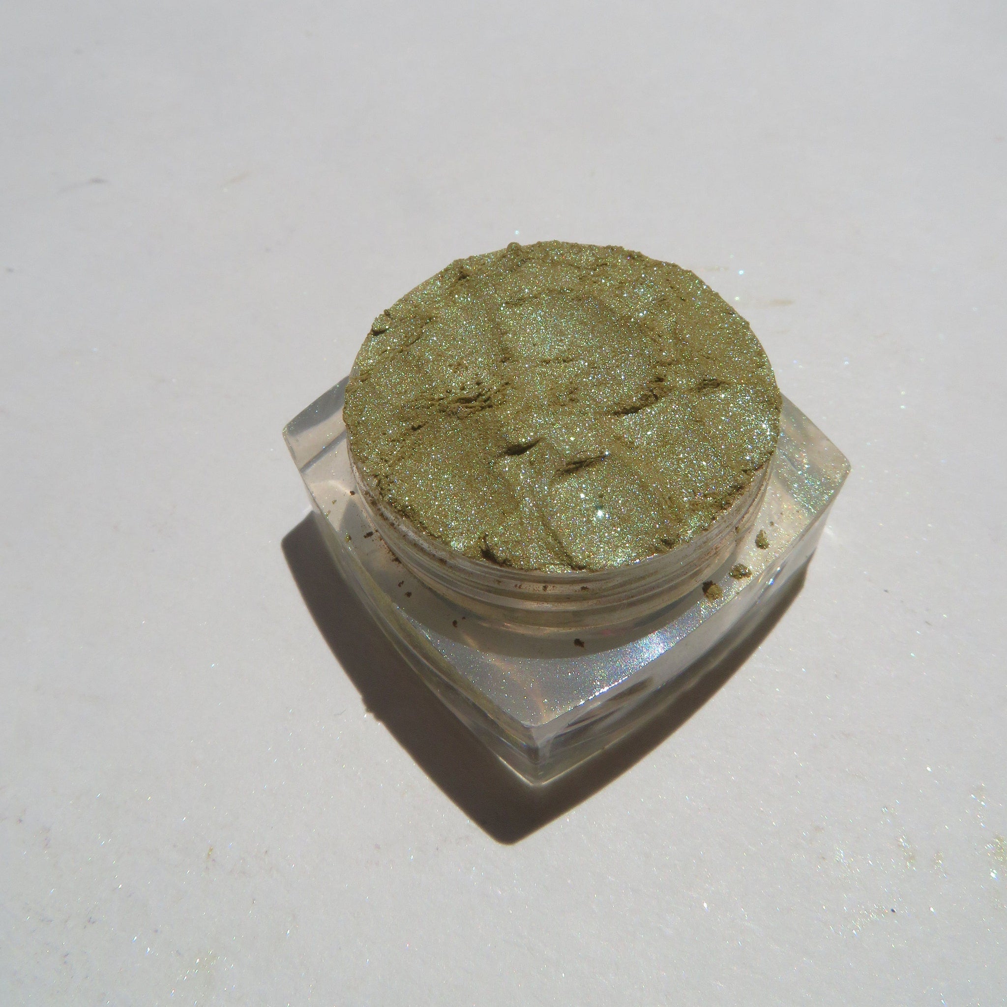 Hand applying shimmering green and gold vegan mineral eyeshadow with fingertip for bold eye look