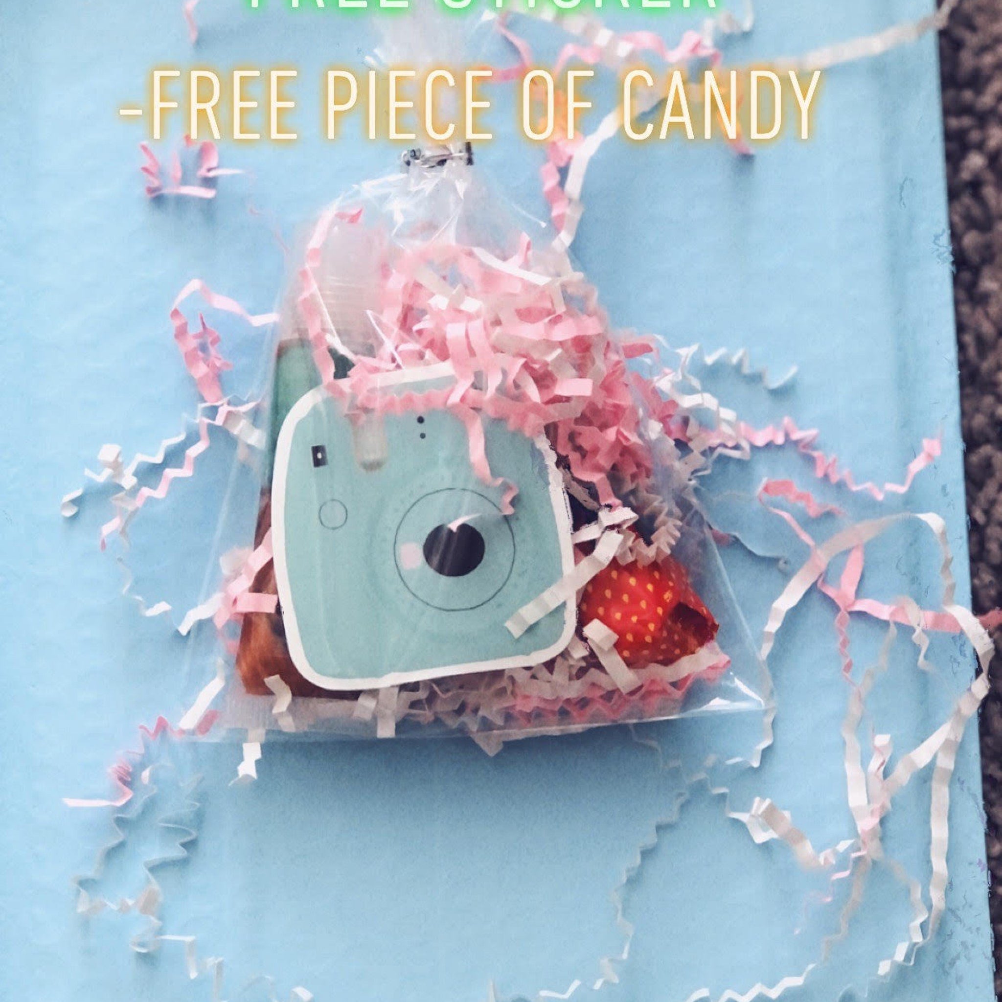 Candy bag with blue camera sticker, pink and white paper shreds, and red strawberry candy on blue background
