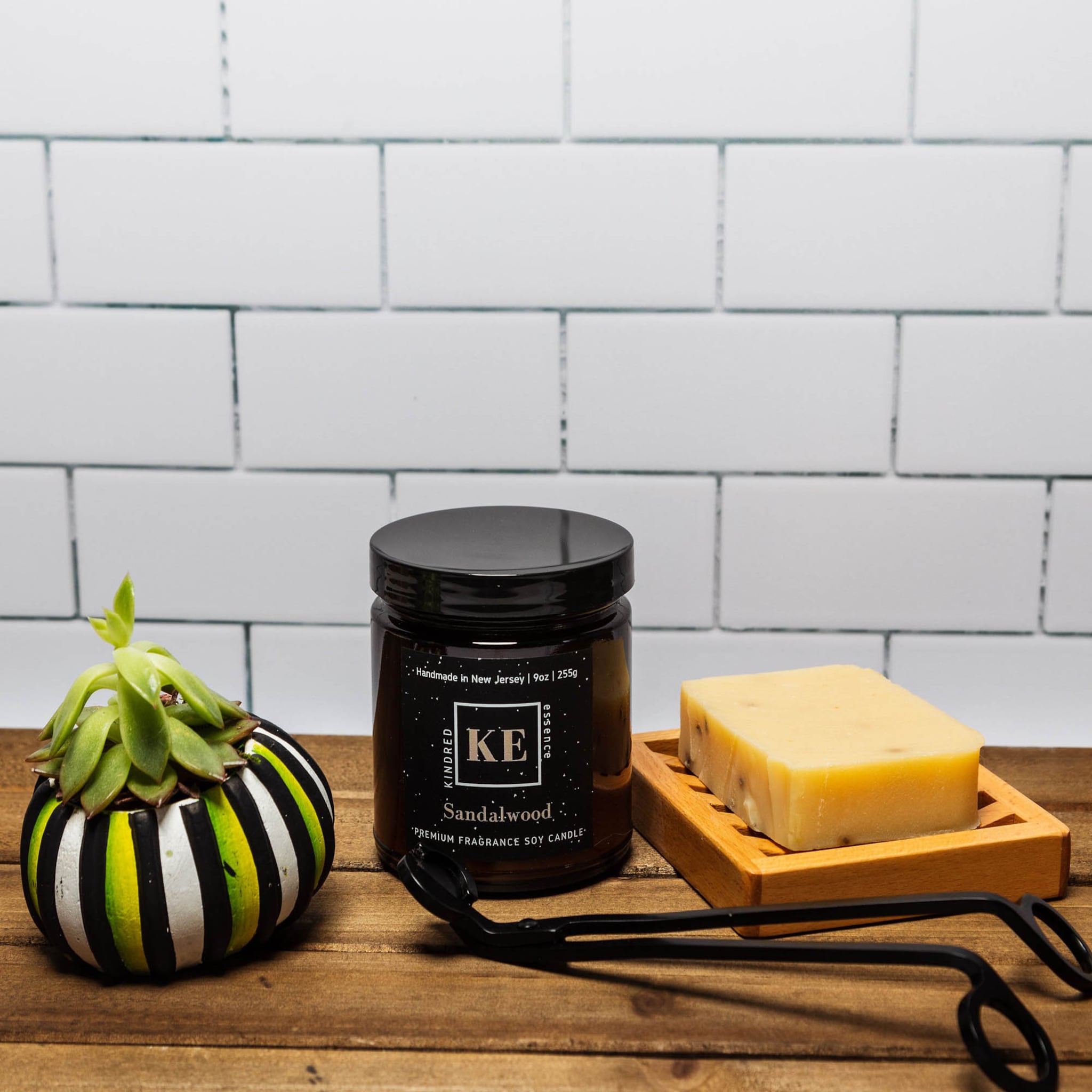Sandalwood candle in a black jar, with a wooden soap dish, on a wooden surface