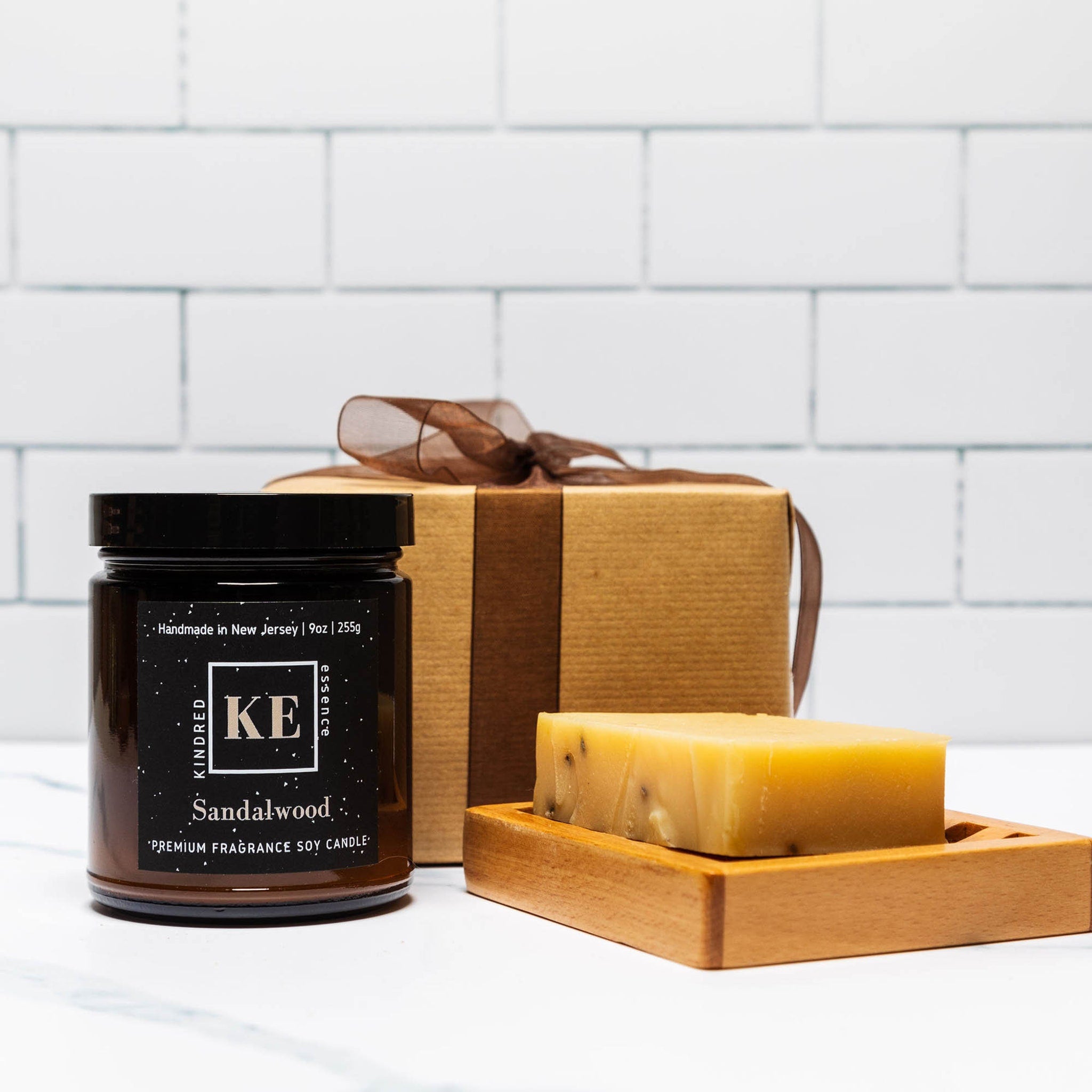 Sandalwood candle in a black jar with brown lid, soap, and gift box with ribbon