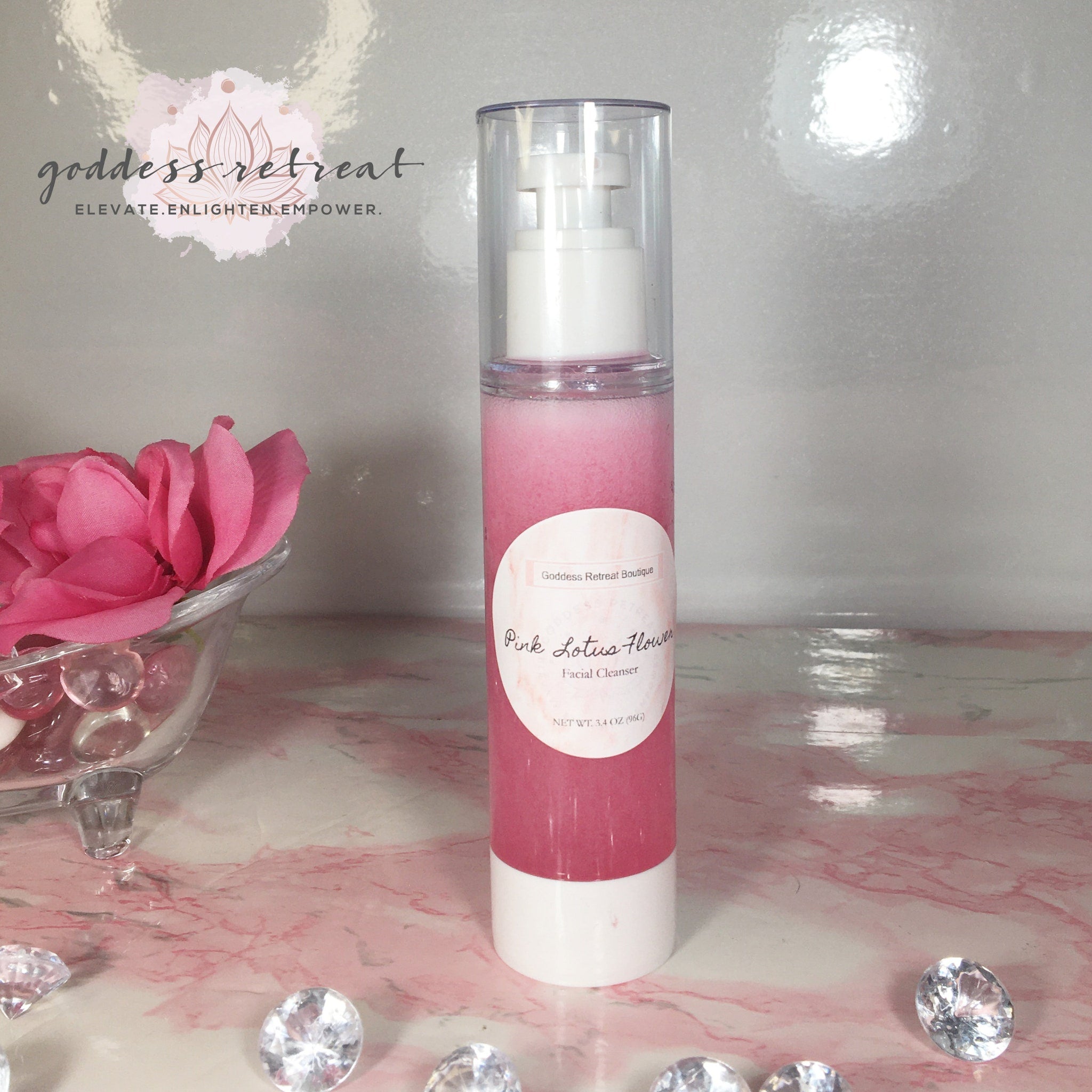 Facial cleanser bottle with pink liquid and white pump, on pink marble surface with diamonds, Goddess Retreat brand