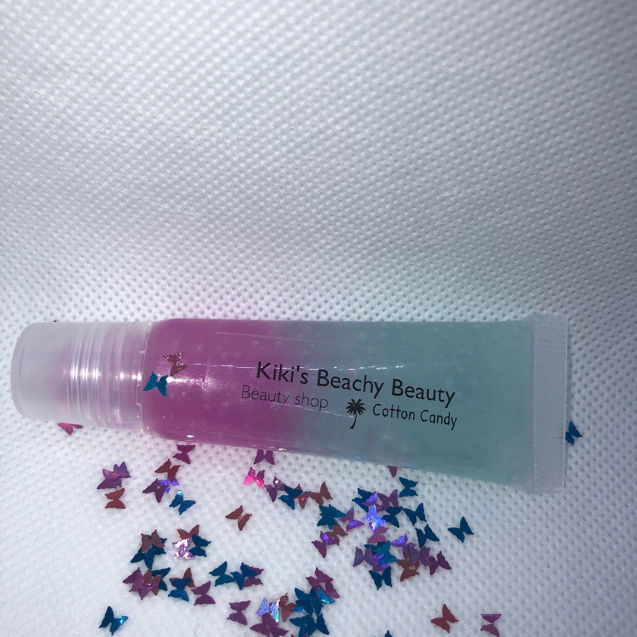 Lip gloss tube with pink and blue gradient, clear tube, and butterfly confetti, Kiki's Beachy Beauty brand