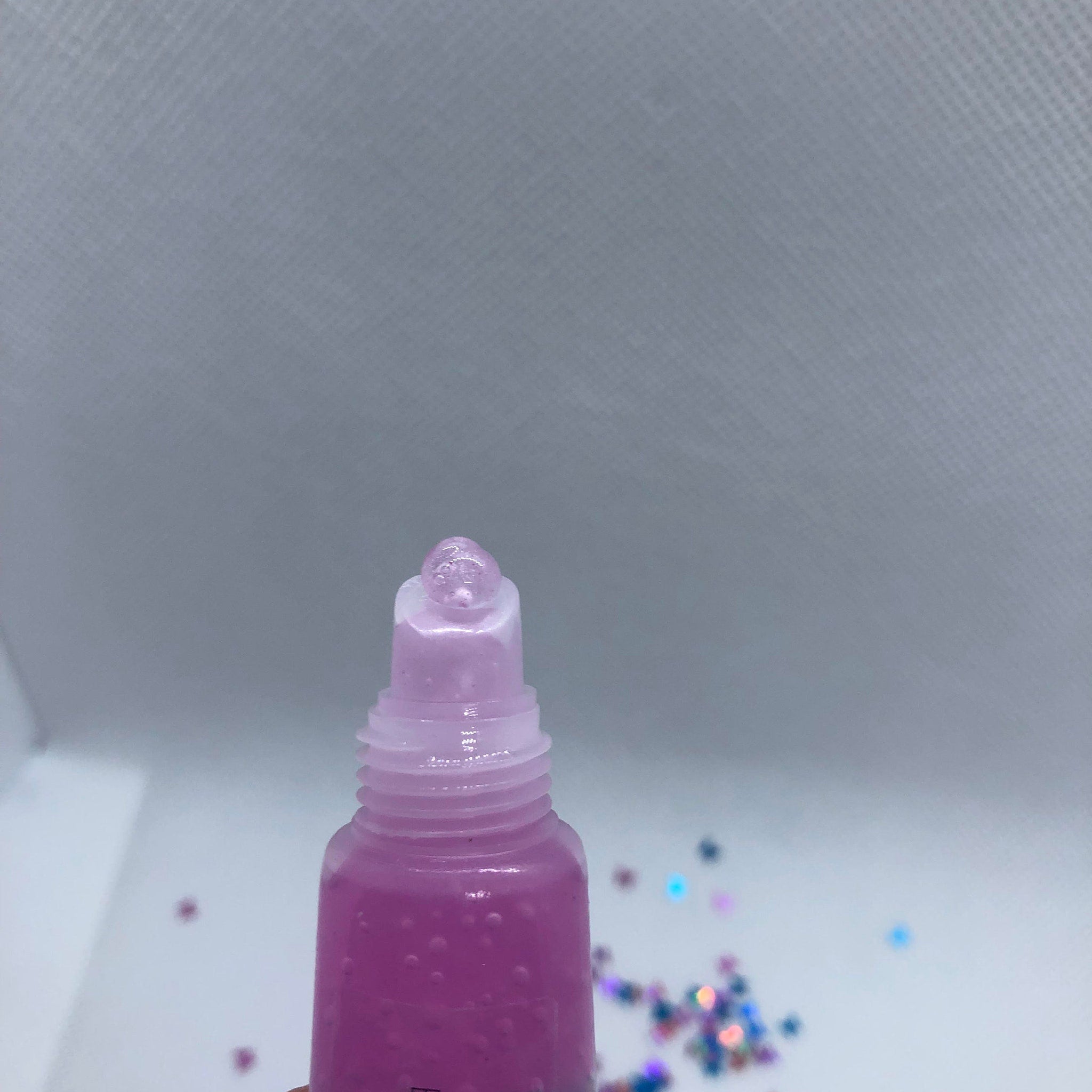 Lip gloss tube with purple liquid, clear applicator, and small bubbles visible inside