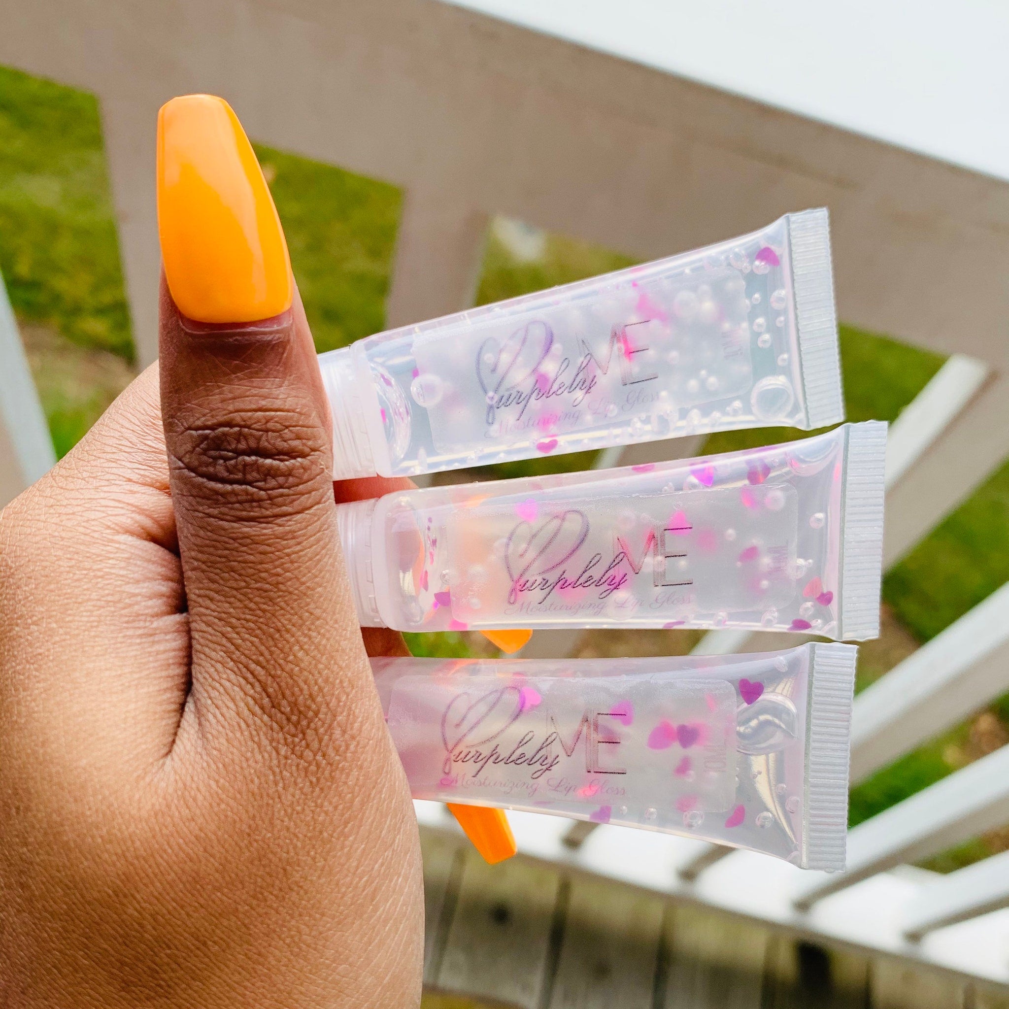 Lip gloss tubes with clear plastic, pink heart accents, and "Purpleby ME" text