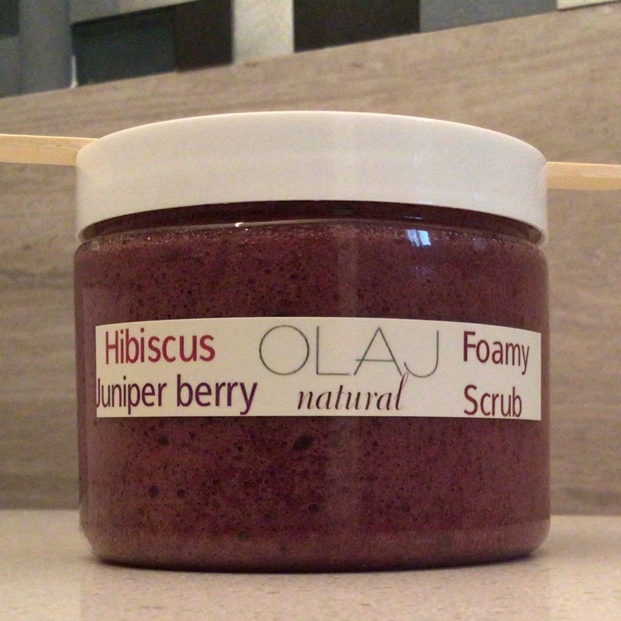 Foamy scrub in a clear jar with white lid, OLAJ label and purple contents