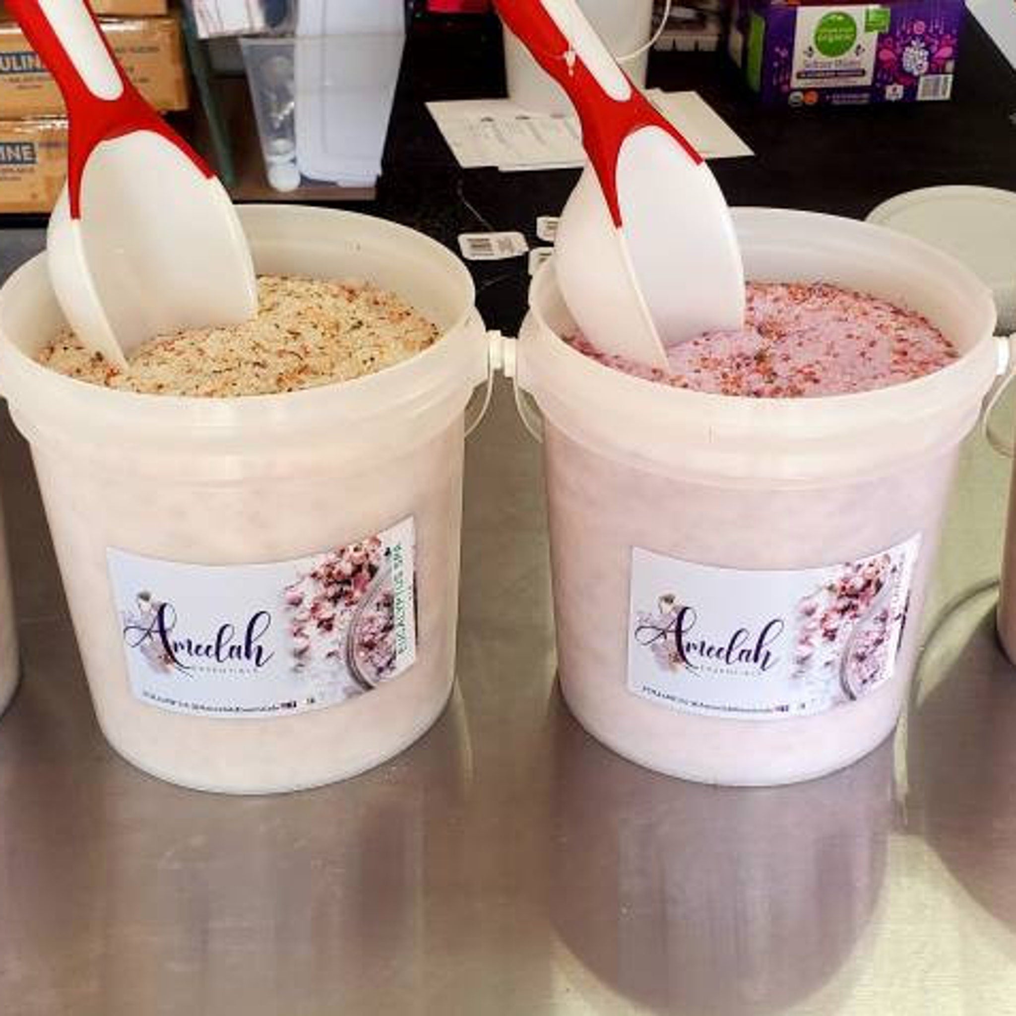 Ameelah Essentials bath salts in pink and beige, with white scoop in tubs on table
