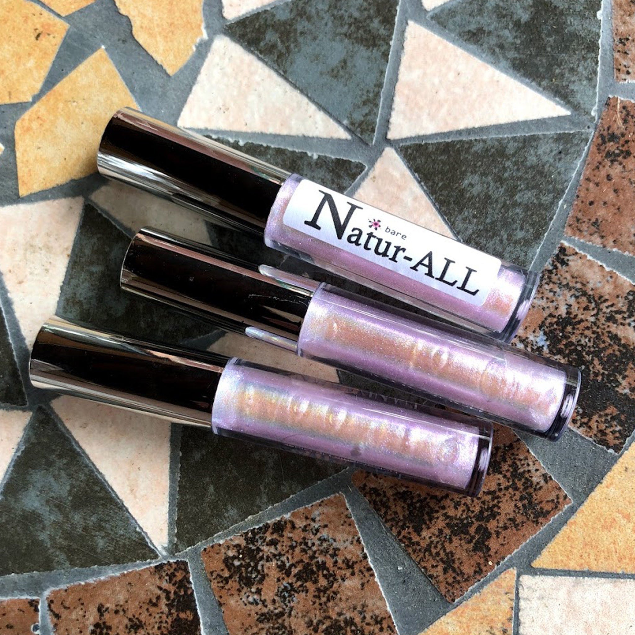 Lip gloss tubes with silver caps, iridescent pink gloss, and Natur-ALL label