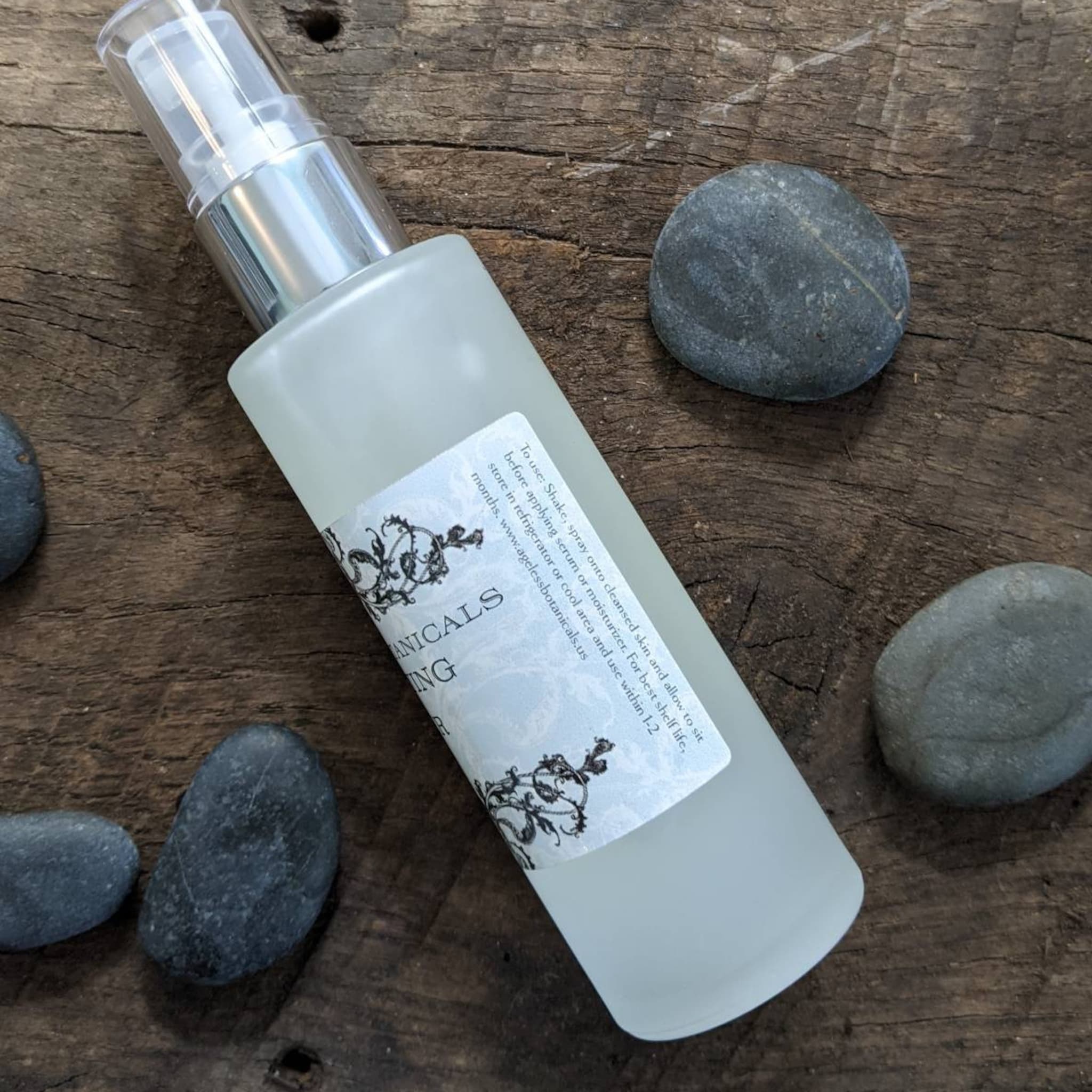 Spray bottle with clear glass, silver pump, and Ageless Botanicals label on wood surface